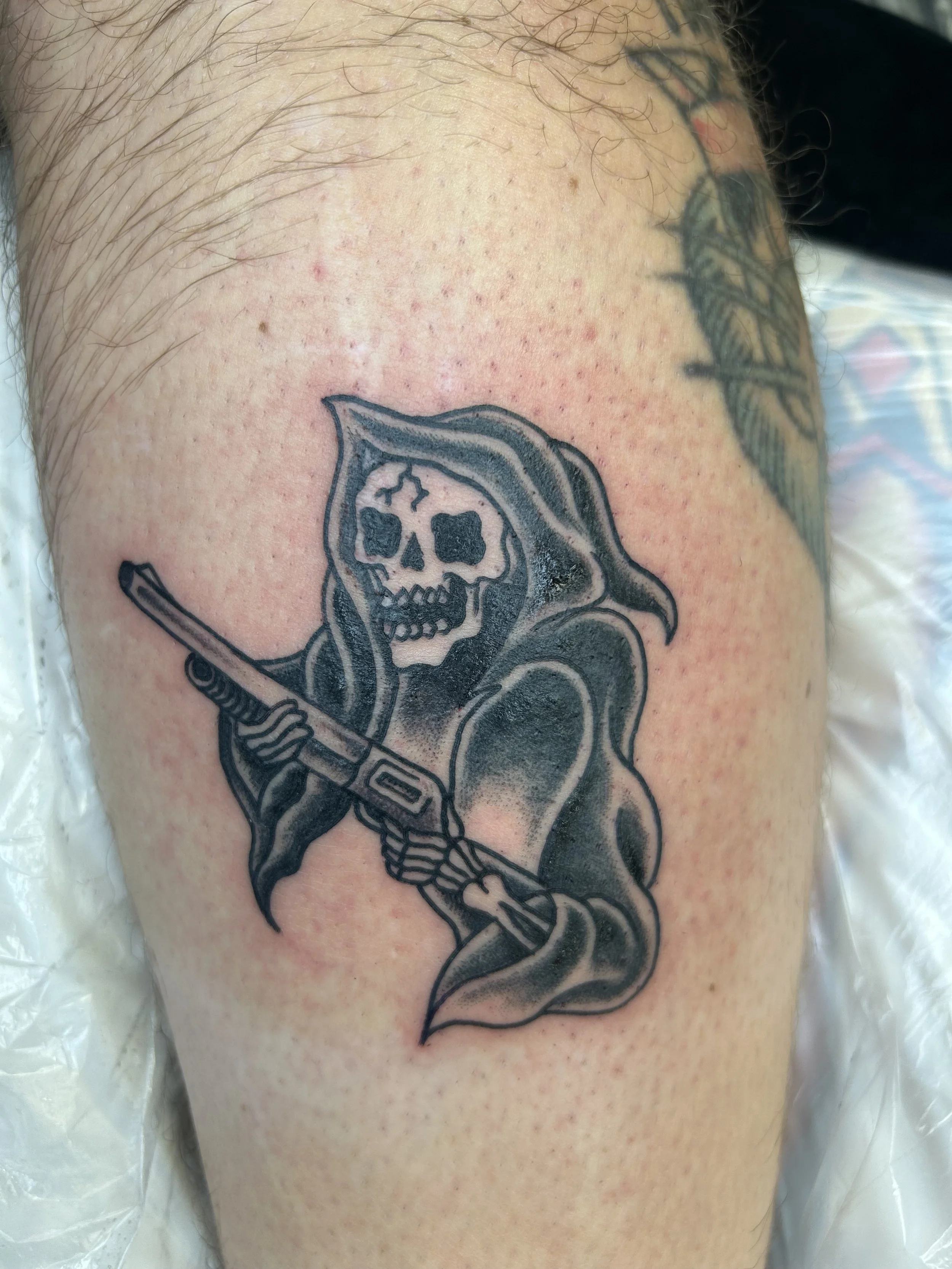 A tattoo of a skeleton wearing a hood and holding a scythe on a person's skin.