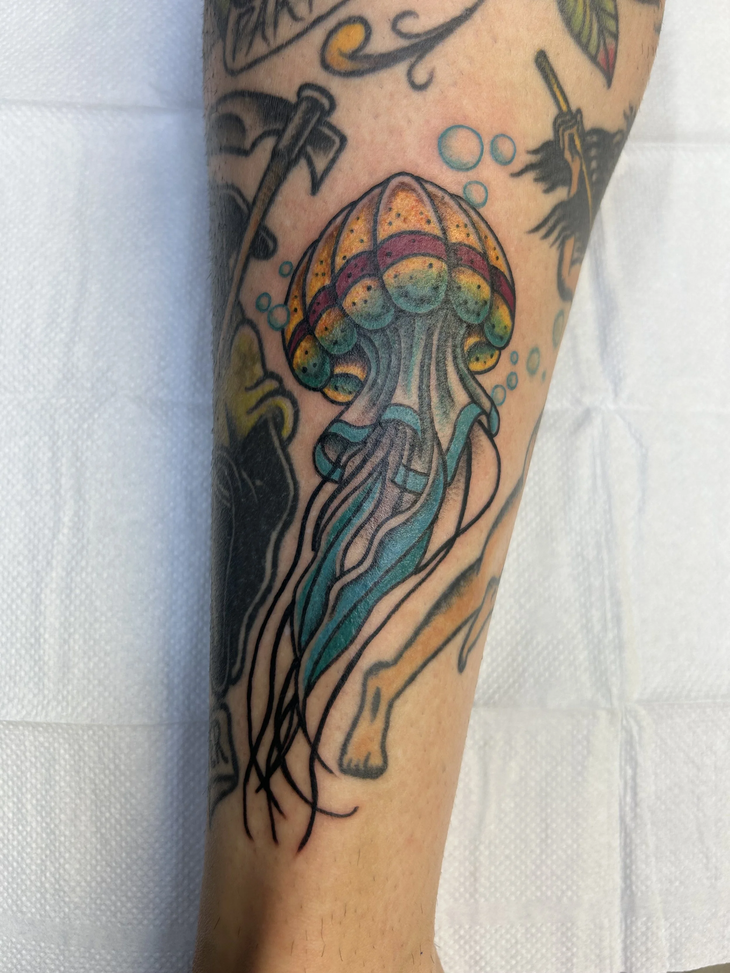 Colorful tattoo of a jellyfish on a person's arm, with bubbles around it and surrounding ocean-themed elements.