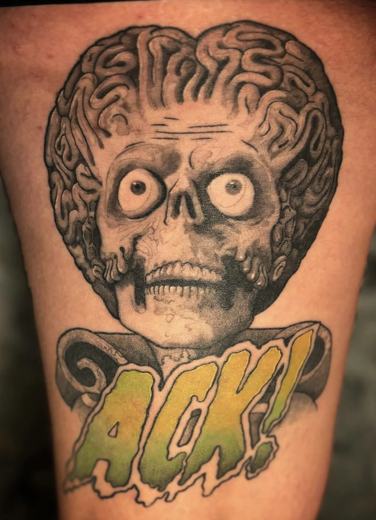 Tattoo of a skull with a brain on top and a green and yellow Monster energy drink logo at the bottom.