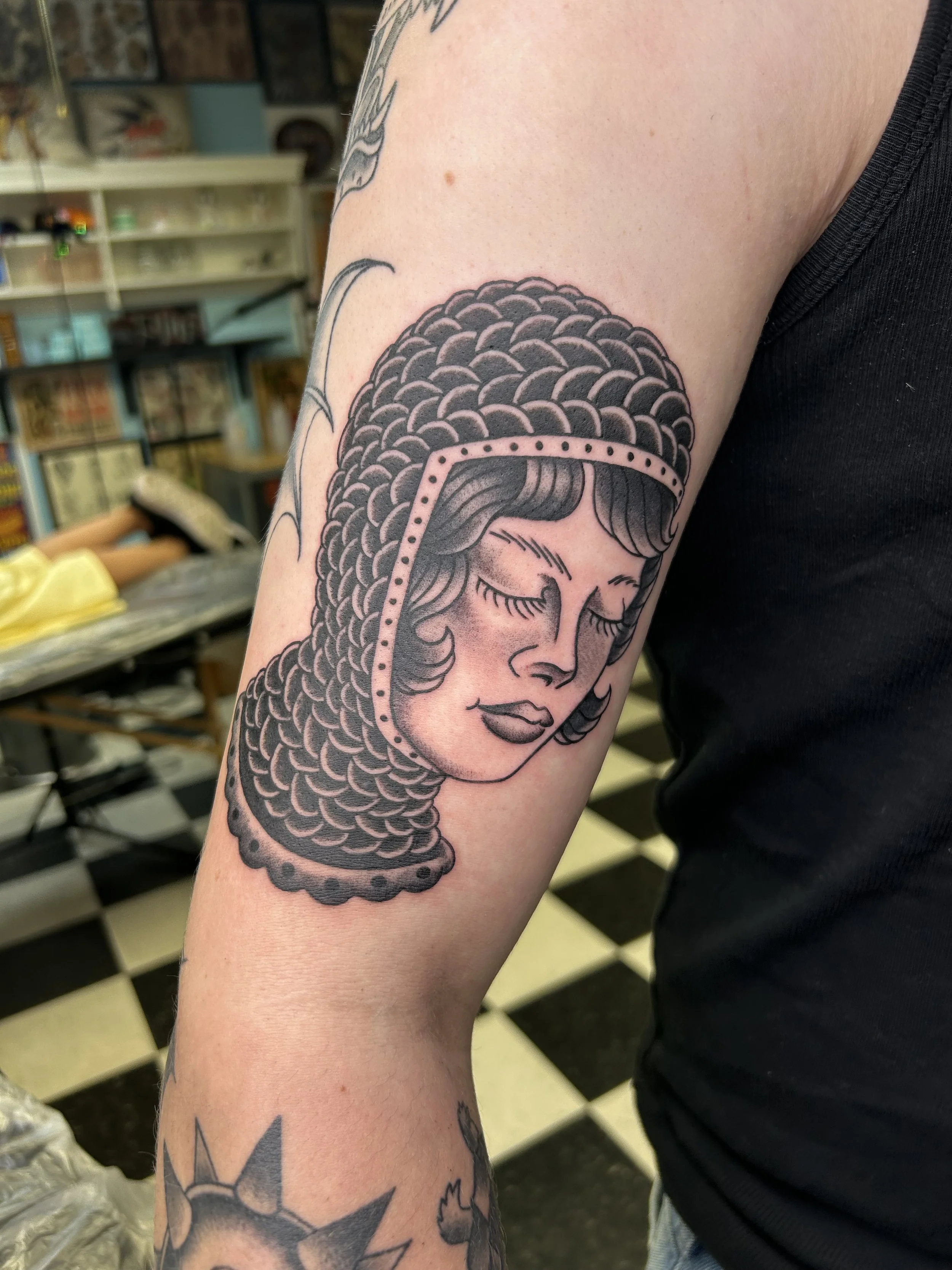 Tattoo of a woman's face with closed eyes, framed by detailed hair and head covering, on a person's arm.