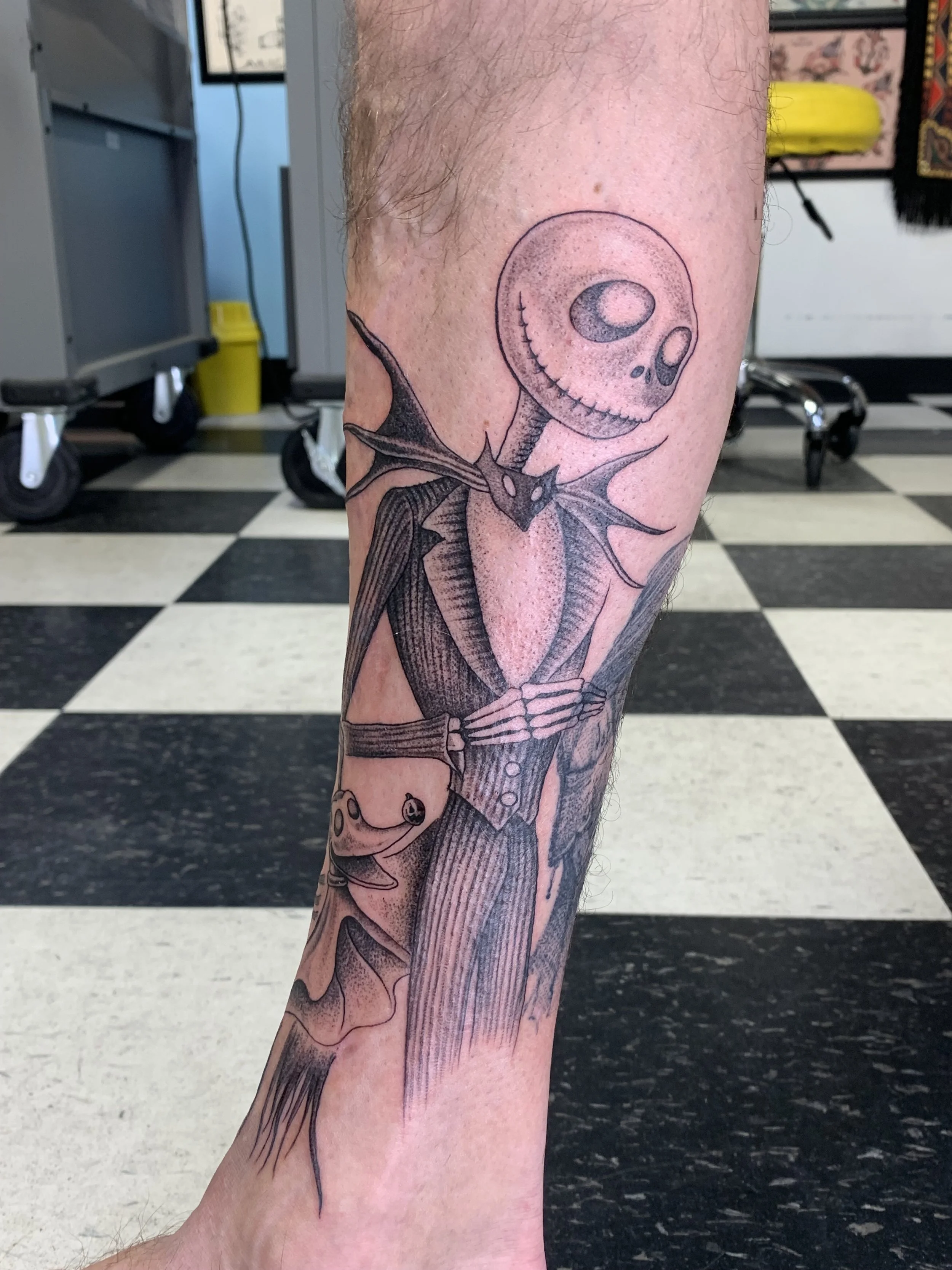 Tattoo of a skeleton holding a large sword on a person's forearm, with a cartoonish skull head with large eye sockets and a small smile, shaded with dotwork and fine line details.