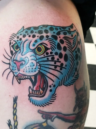 Close-up of a colorful tiger tattoo on skin, with blue and black markings, yellow eyes, and open mouth showing teeth.