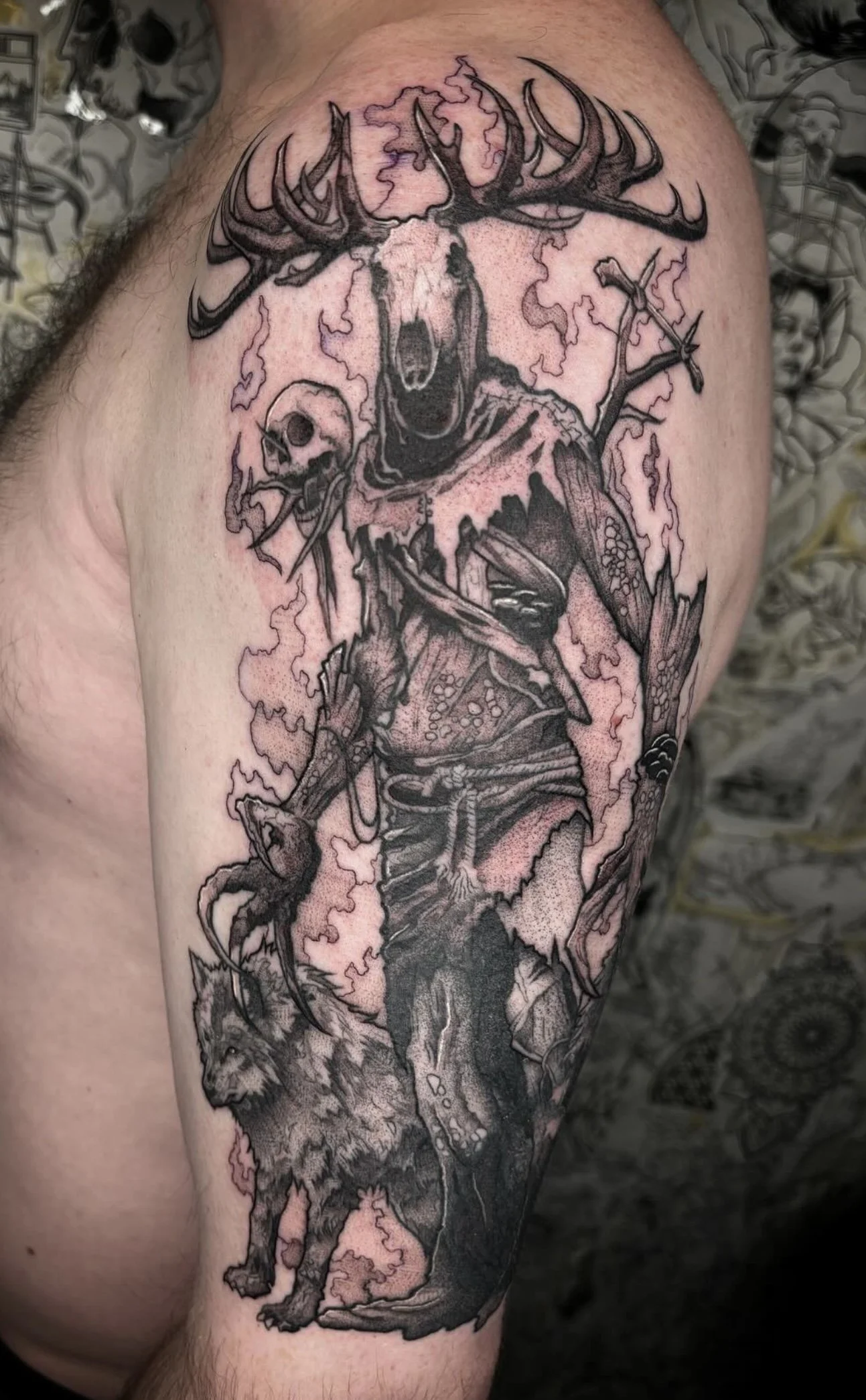 Tattoo of a creature with the body of a wolf, human-like face, and antlers, holding a skull, surrounded by lightning, on a person's arm.