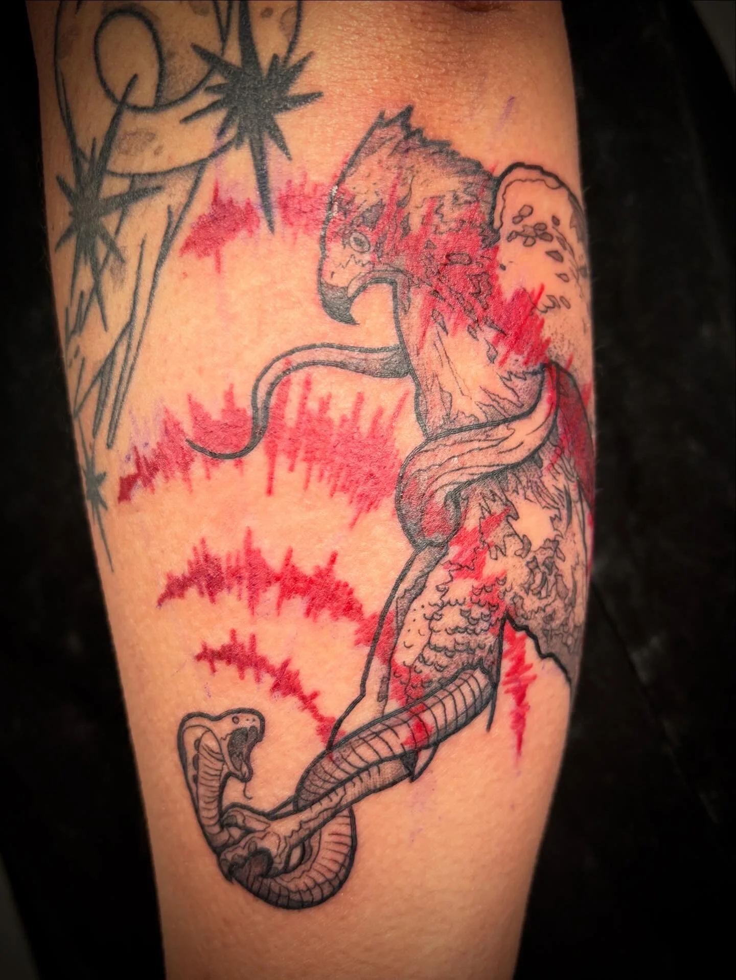 Tattoo of a dragon on a person's arm, with red ink accents and black outline, with some spiky designs above.