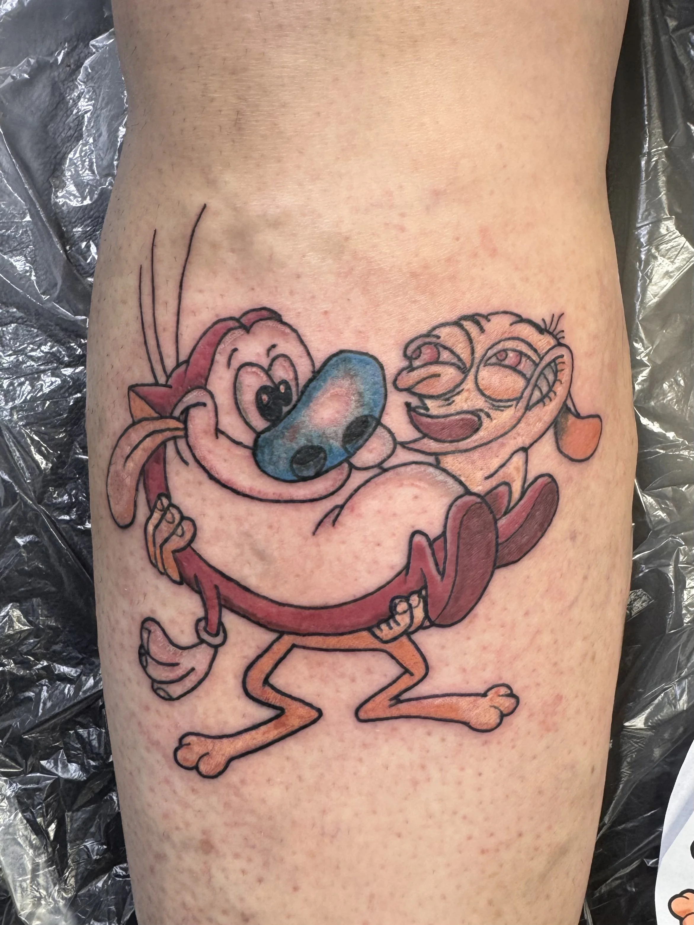 Colorful tattoo of cartoon characters, including a pink octopus, a blue fish, and an orange crab, with the octopus and fish smiling and the crab looking amused, on a person's skin.