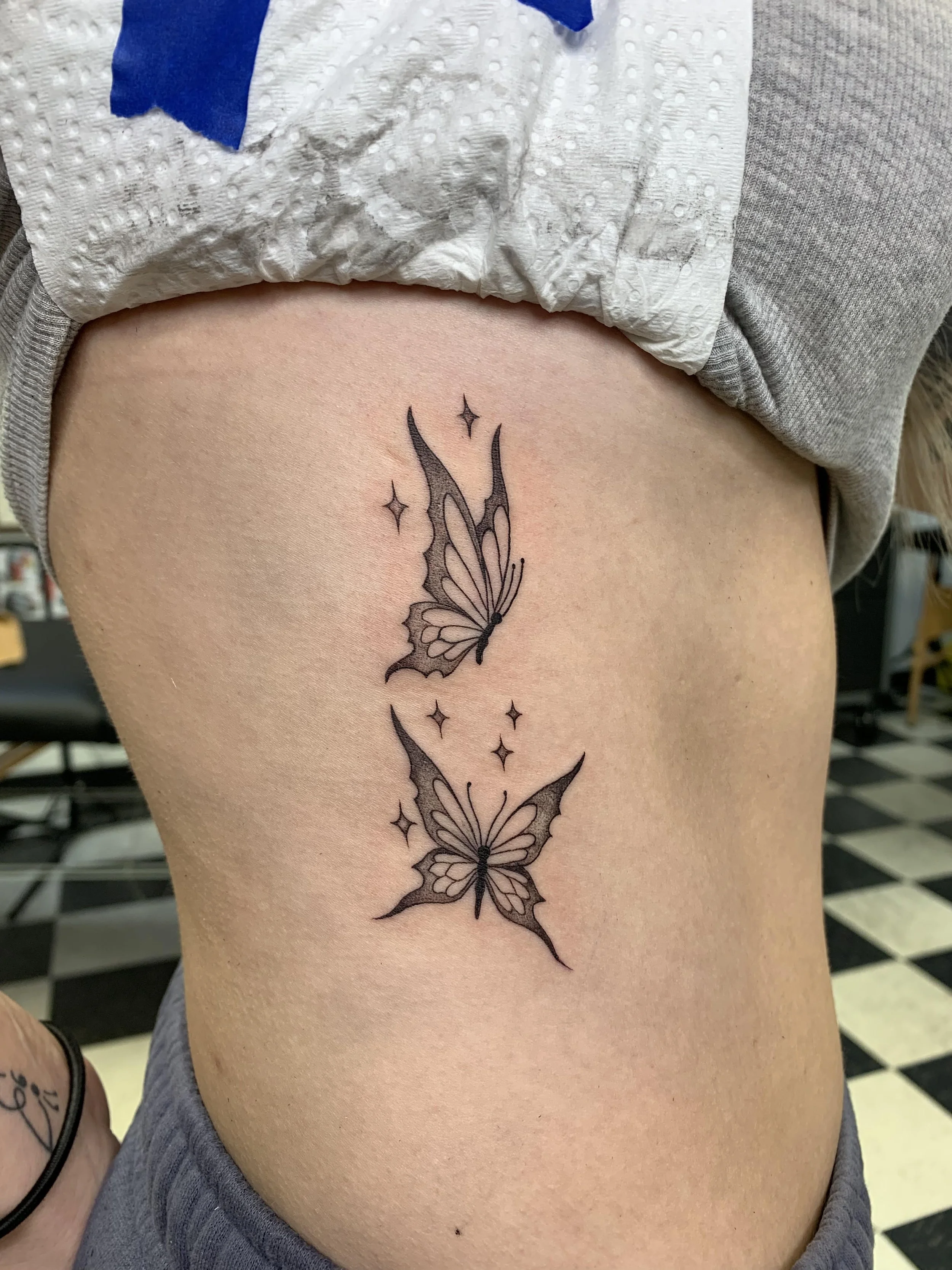 A person's side torso with a tattoo of two butterflies and small stars.