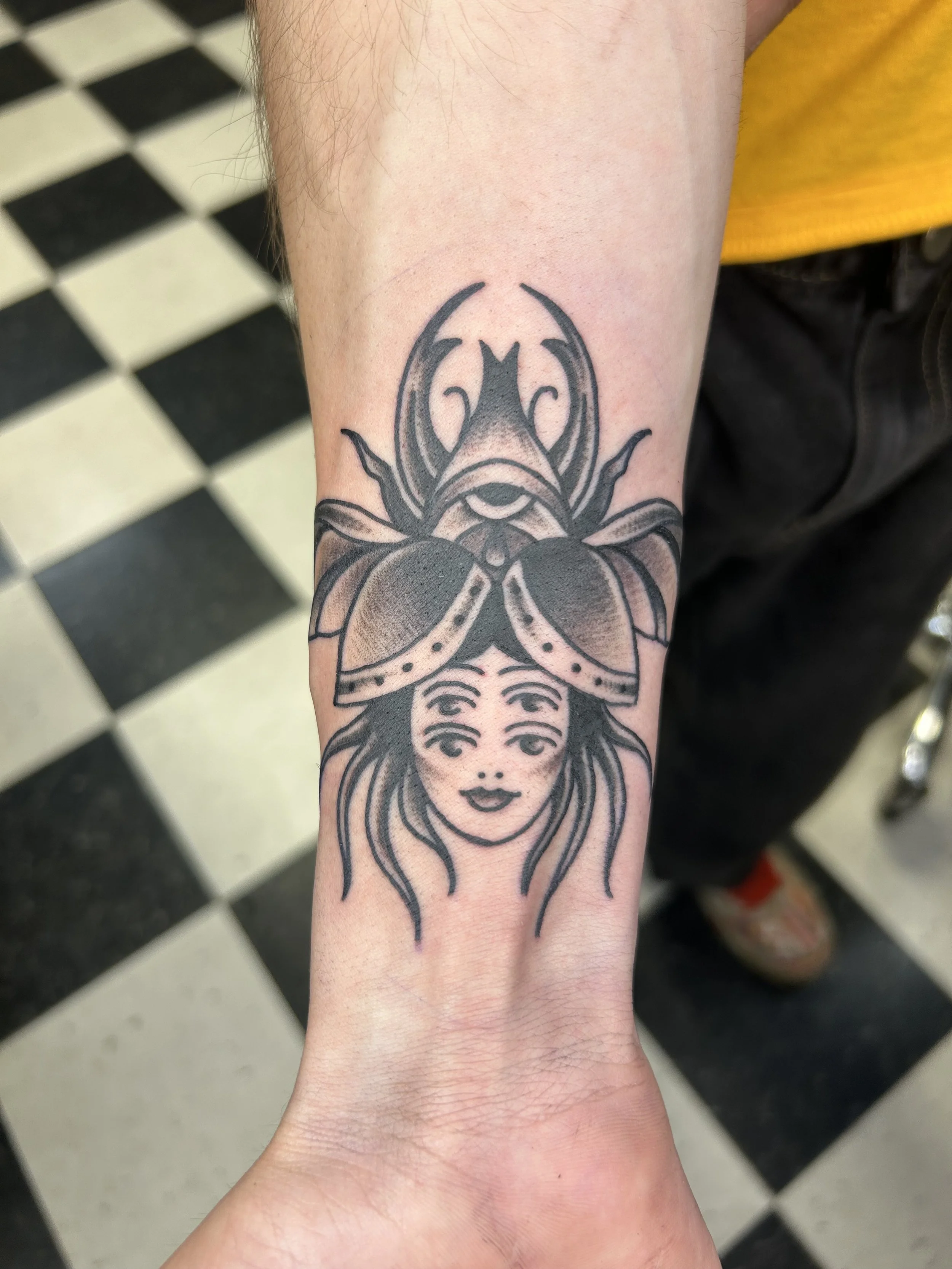 A tattoo on a person's forearm features the image of a butterfly with a woman's face at the bottom. The butterfly's wings are symmetrical with intricate details.