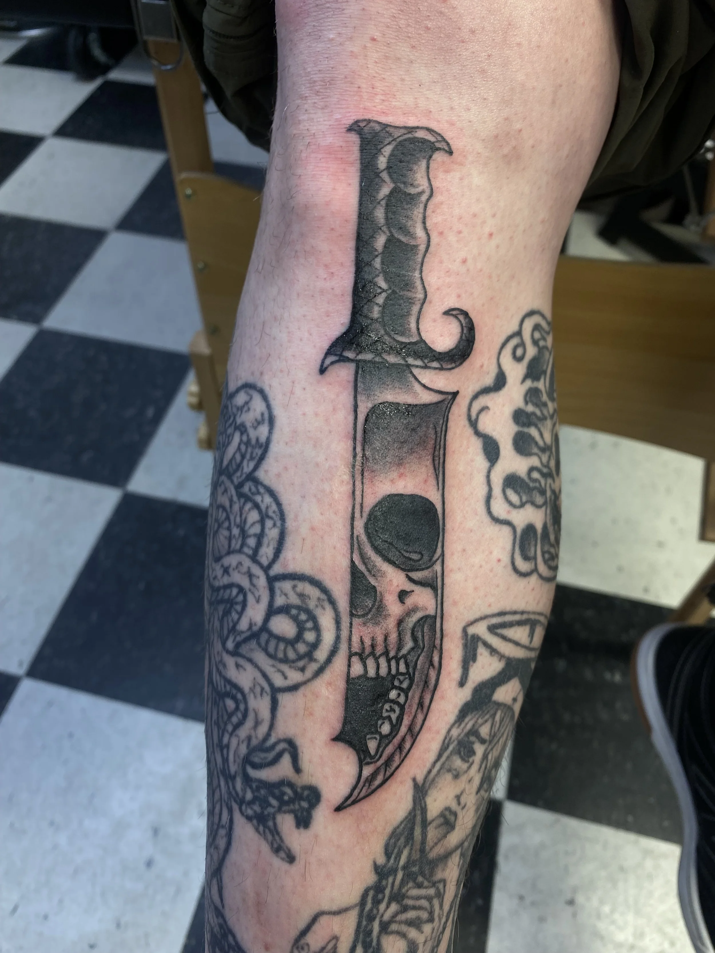A tattoo of a large, detailed pistol on a person's forearm, with additional ink designs visible around it.