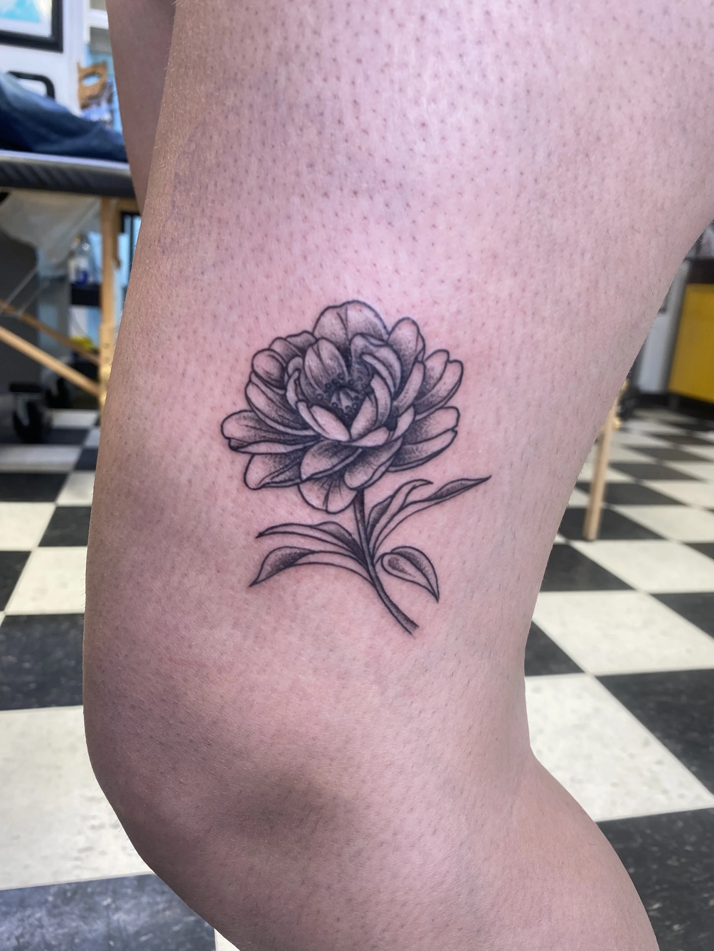 A black and gray line tattoo of a detailed flower on a person's upper leg.