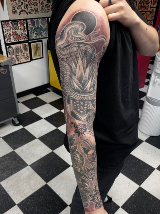 Tattoo of a serpent coiled around a mountain on a person's arm.