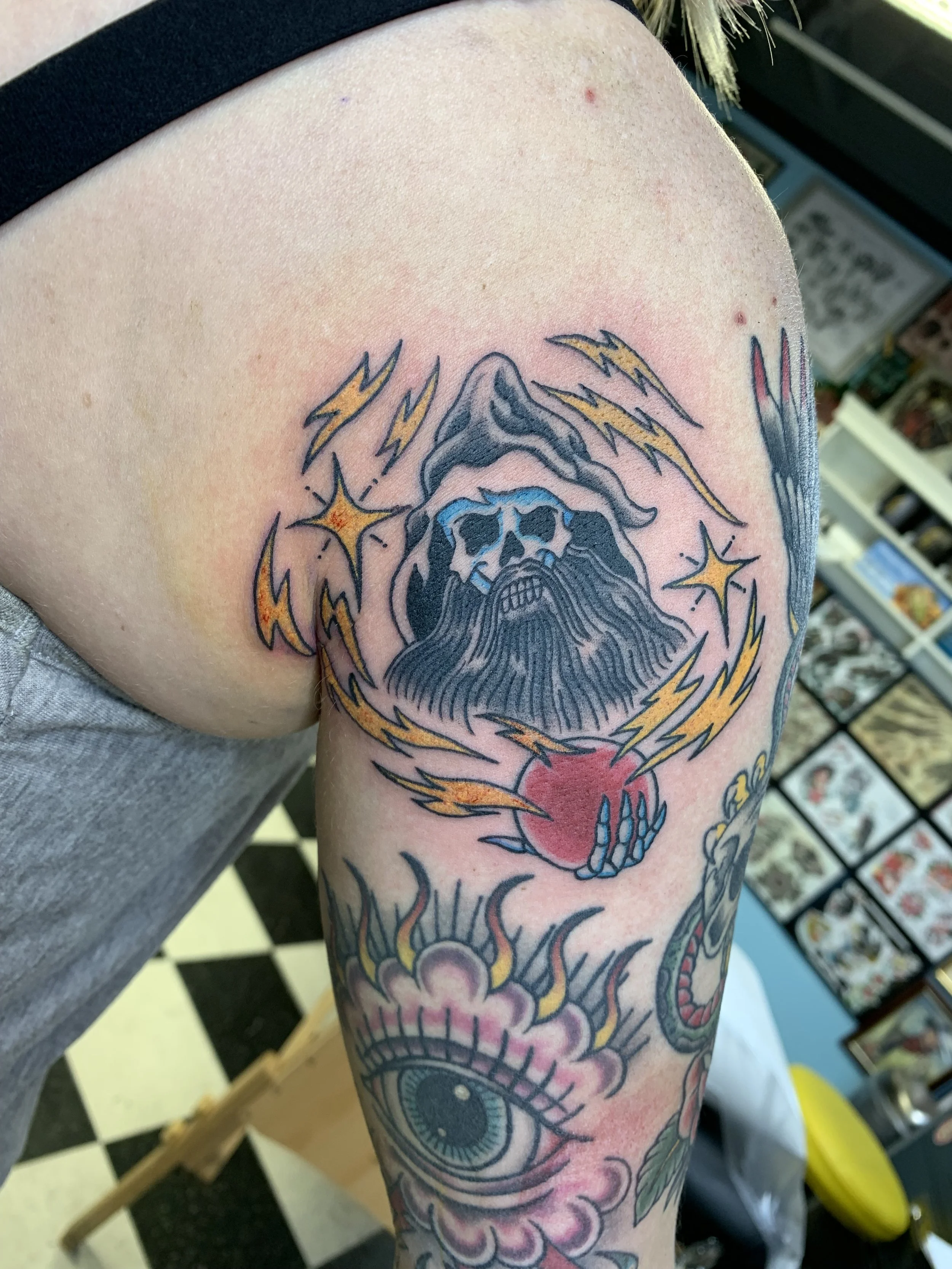 Tattoo of a skull with lightning bolts around it on a person's upper arm.