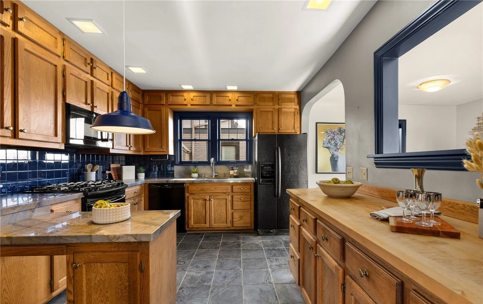 Kitchen with wooden cabinets, black appliances, dark blue tile backsplash, and a window over the sink.