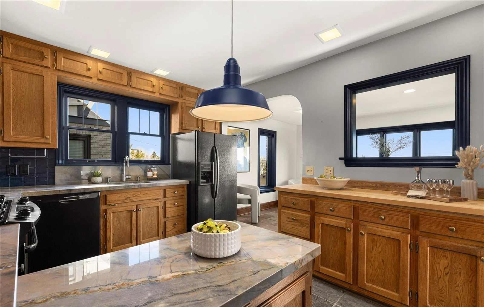 Kitchen with wooden cabinets, black appliances, a marble countertop island with a white bowl of fruit, and a black pendant light hanging above the island.