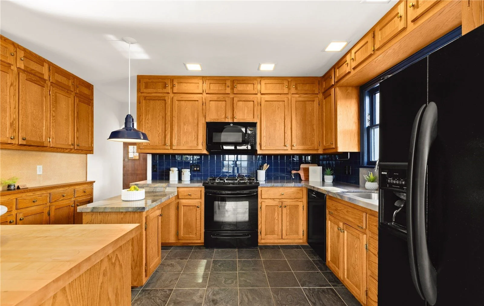 Kitchen with wooden cabinets, black appliances, dark tiled flooring, and a blue tile backsplash.