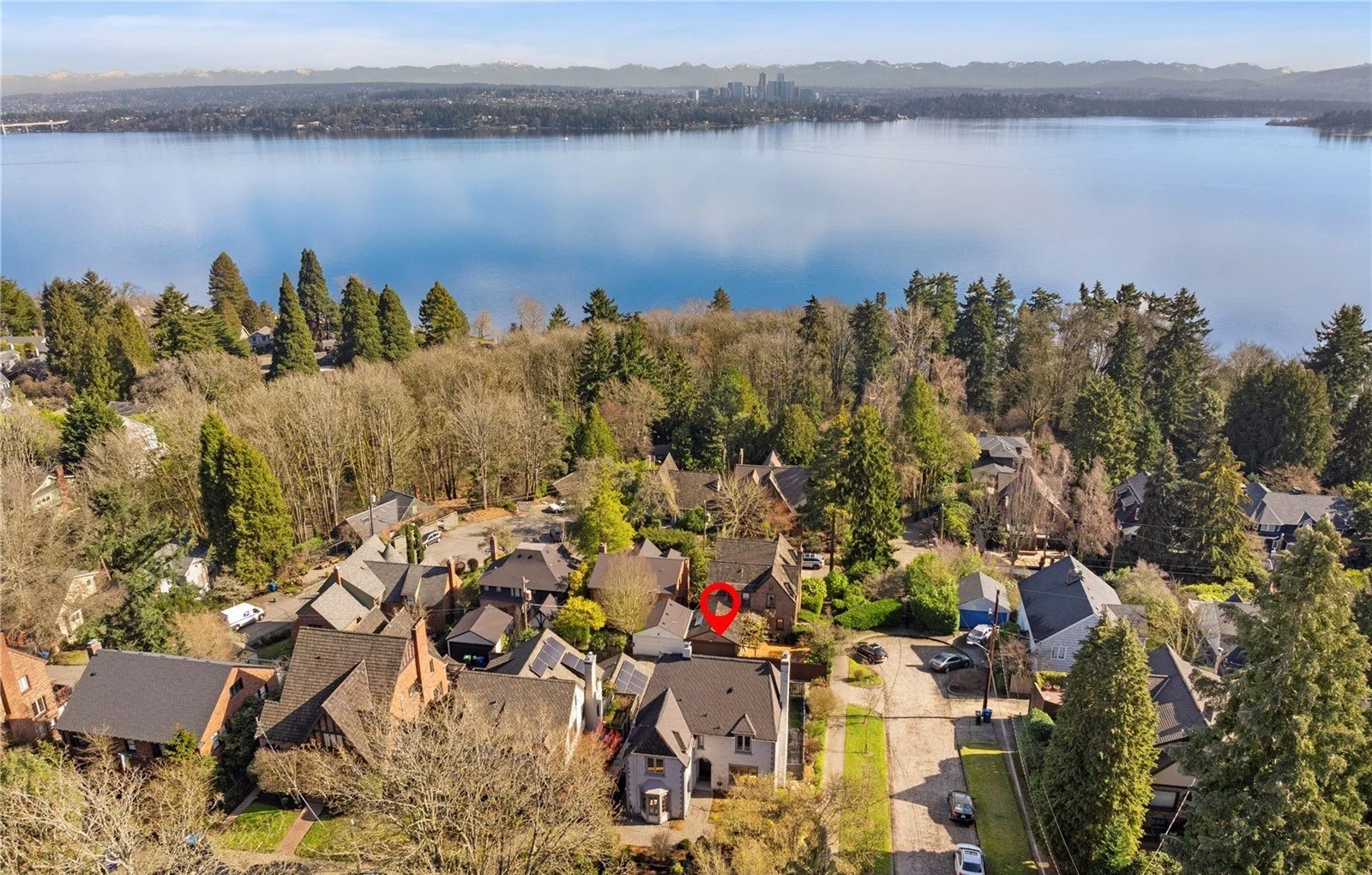 Aerial view of a residential neighborhood near a large body of water with mountains in the background, trees, and houses with varied roofs.