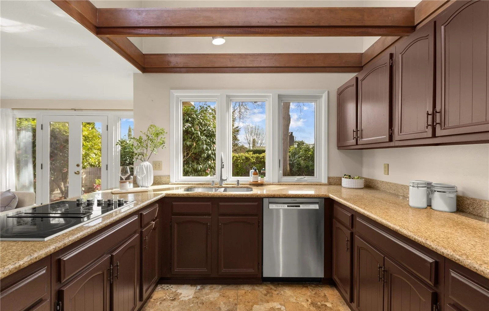Kitchen with brown cabinets, beige granite countertops, and a window overlooking greenery, with a dishwasher and a stovetop.