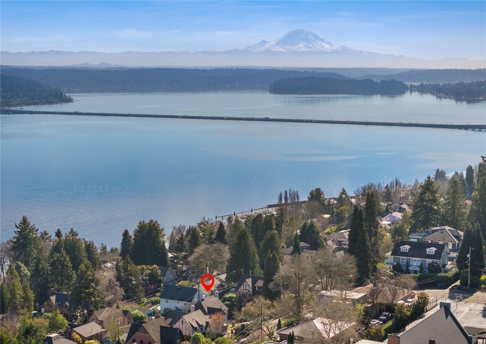 Aerial view of a suburban neighborhood near a large body of water, with a snow-capped mountain in the background.