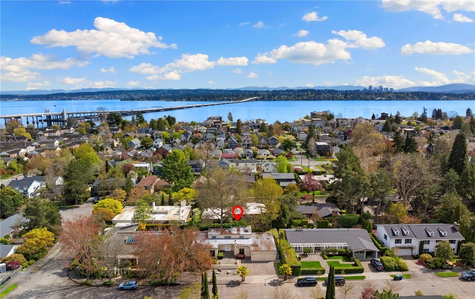 Aerial view of a residential neighborhood near a large body of water with a bridge in the background, under a partly cloudy sky.