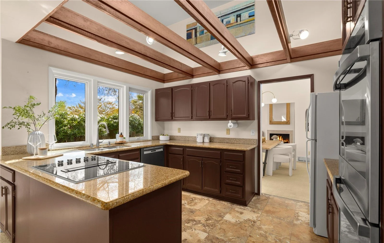 Kitchen with brown cabinets, granite countertops, stainless steel appliances, and three large windows showing greenery outside.