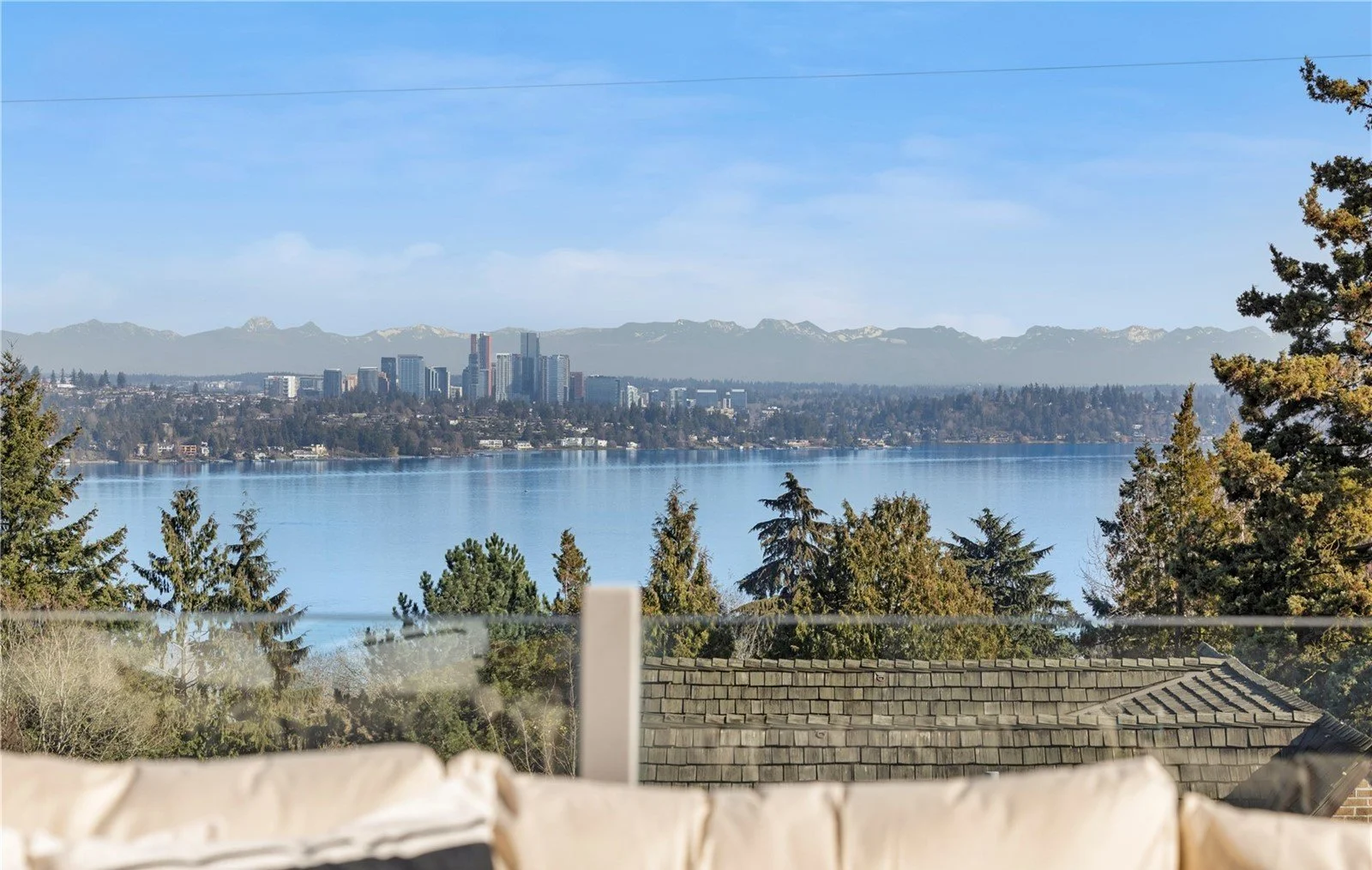 View of a city skyline across a body of water with mountains in the background and trees in the foreground.