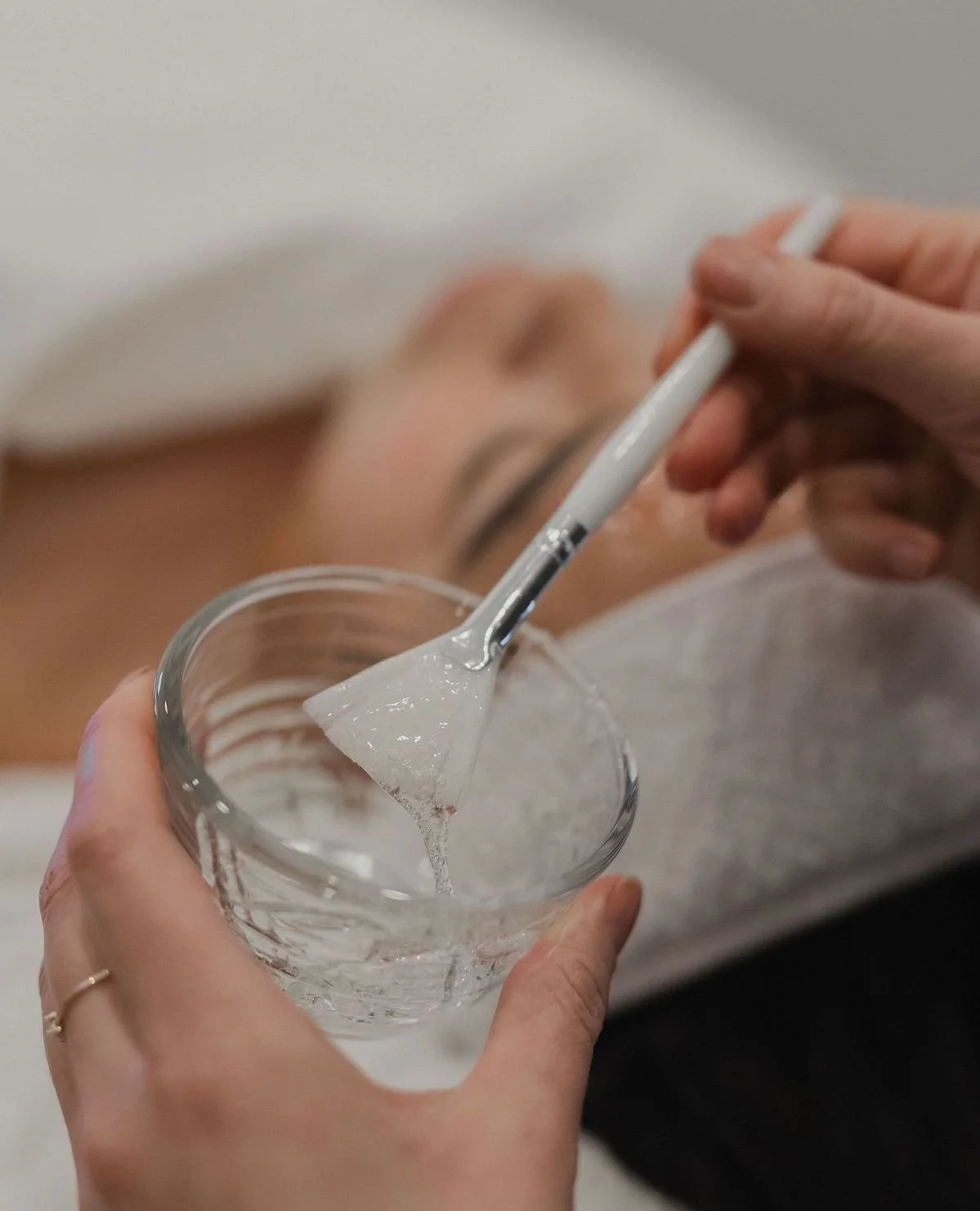 Person lying in bed with eyes closed, holding a glass of water and a thermometer, preparing to take temperature.