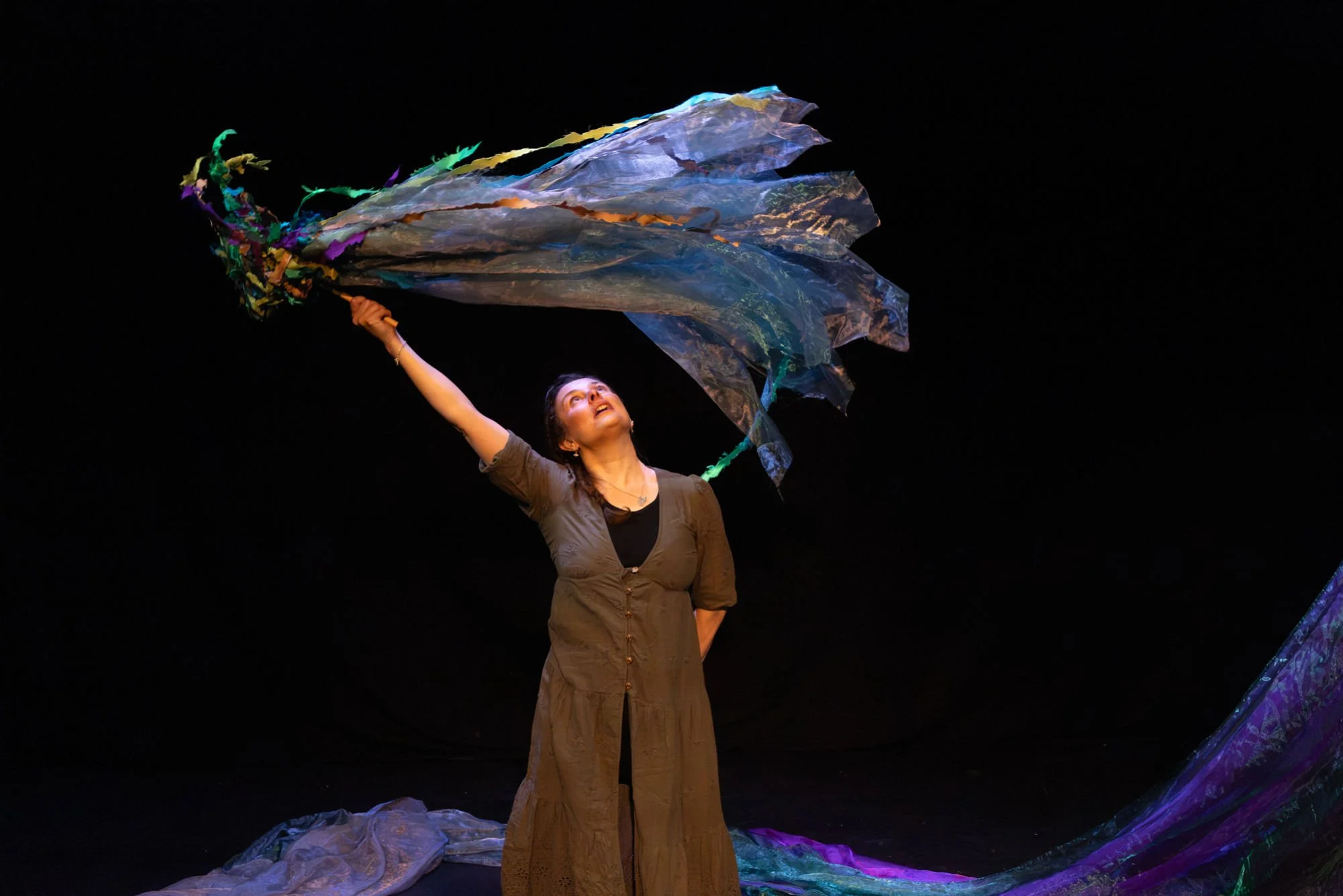 A woman holding a colorful, large fabric puppet above her head on a dark stage.