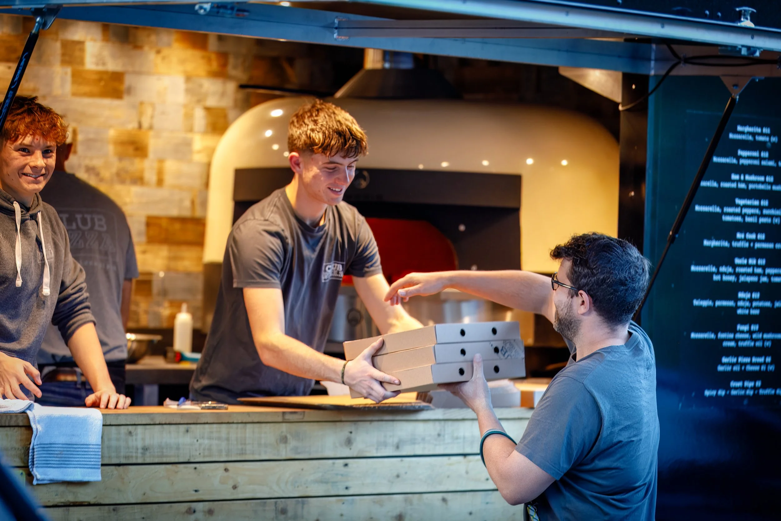 Smiling Club Pizza staff handing over fresh pizzas to one happy customer