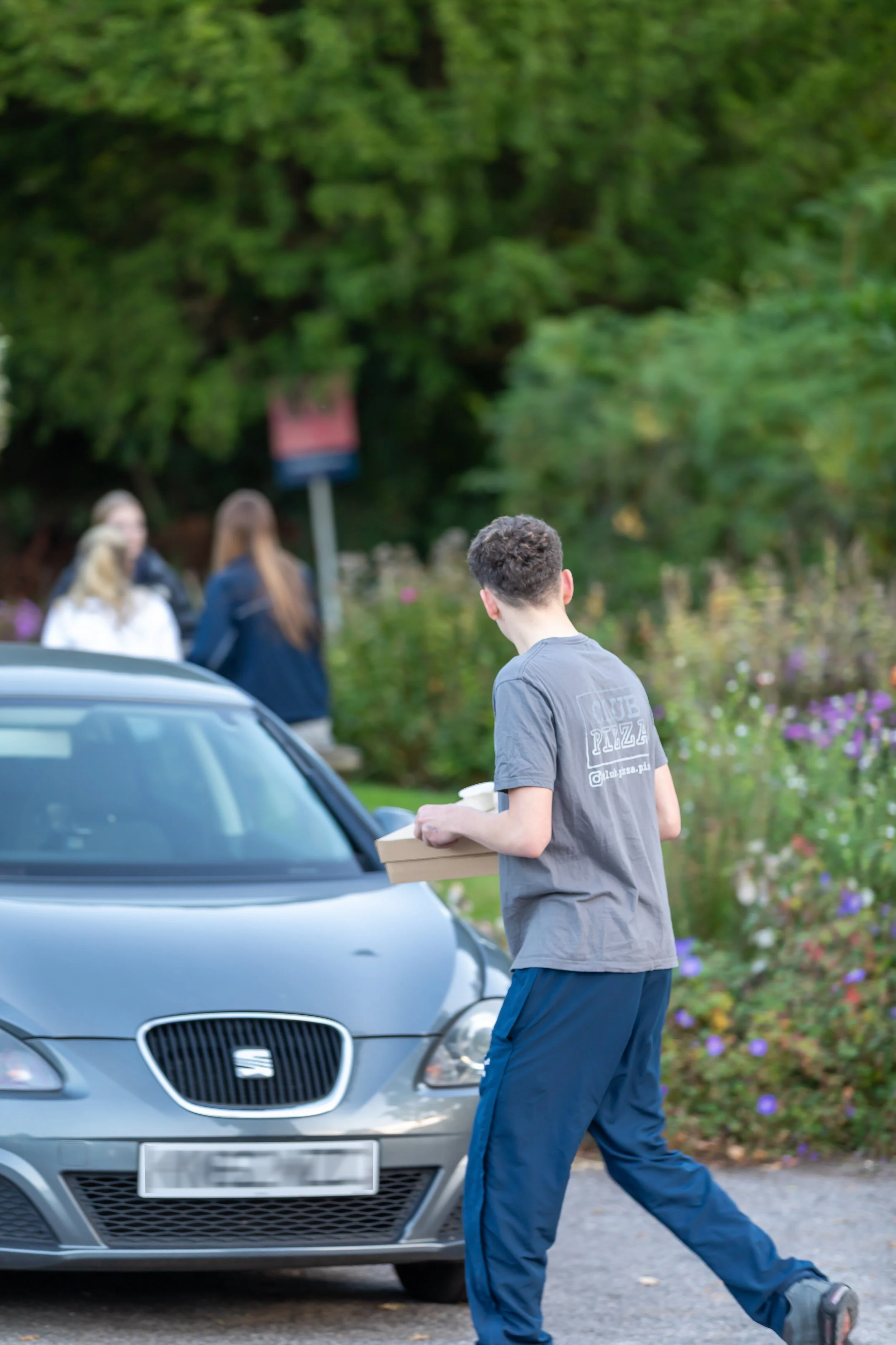 Staff member delivering pizzas to customers waiting in car at Club Pizza