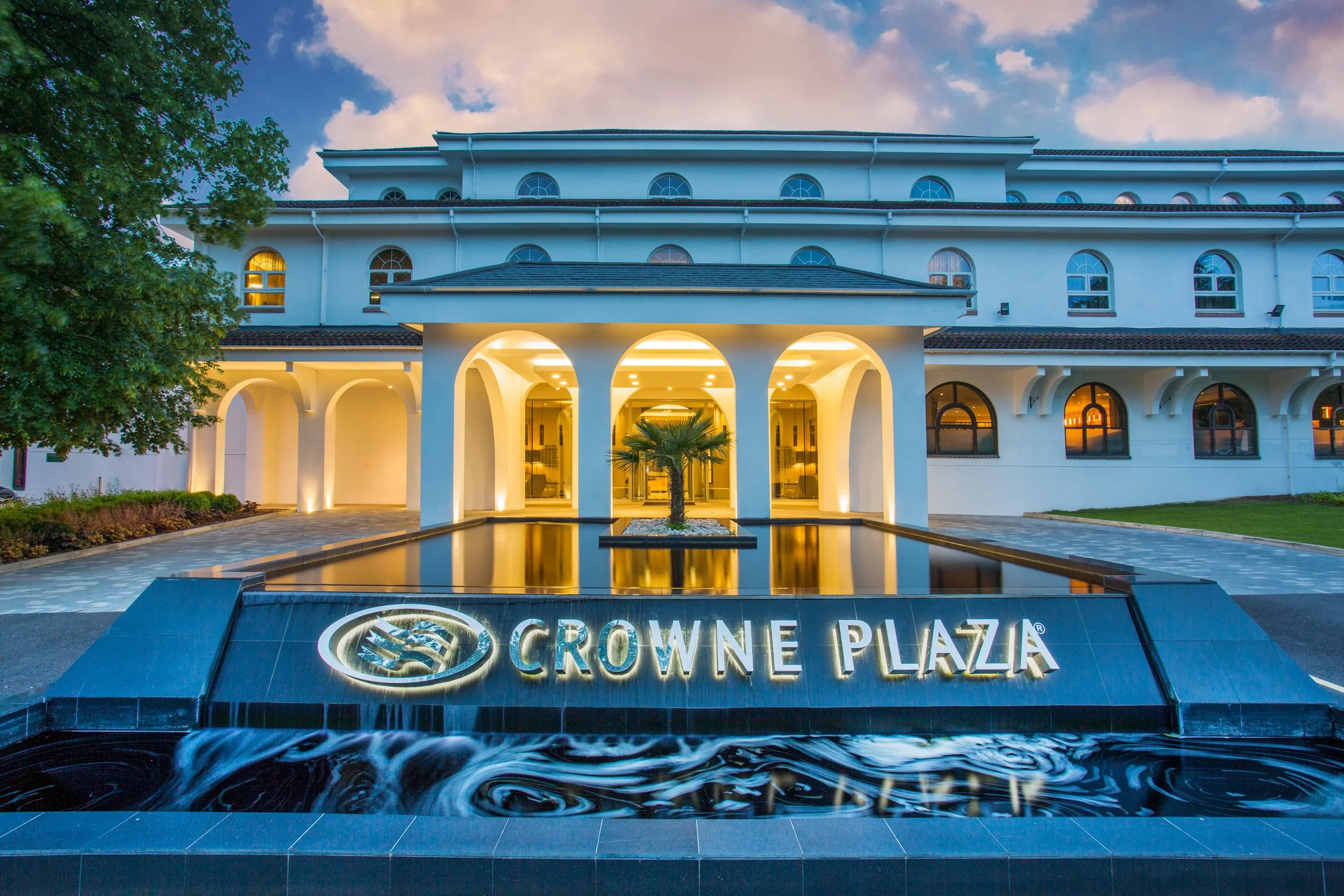 Evening exterior of Crowne Plaza hotel and fountain in Gerrards Cross