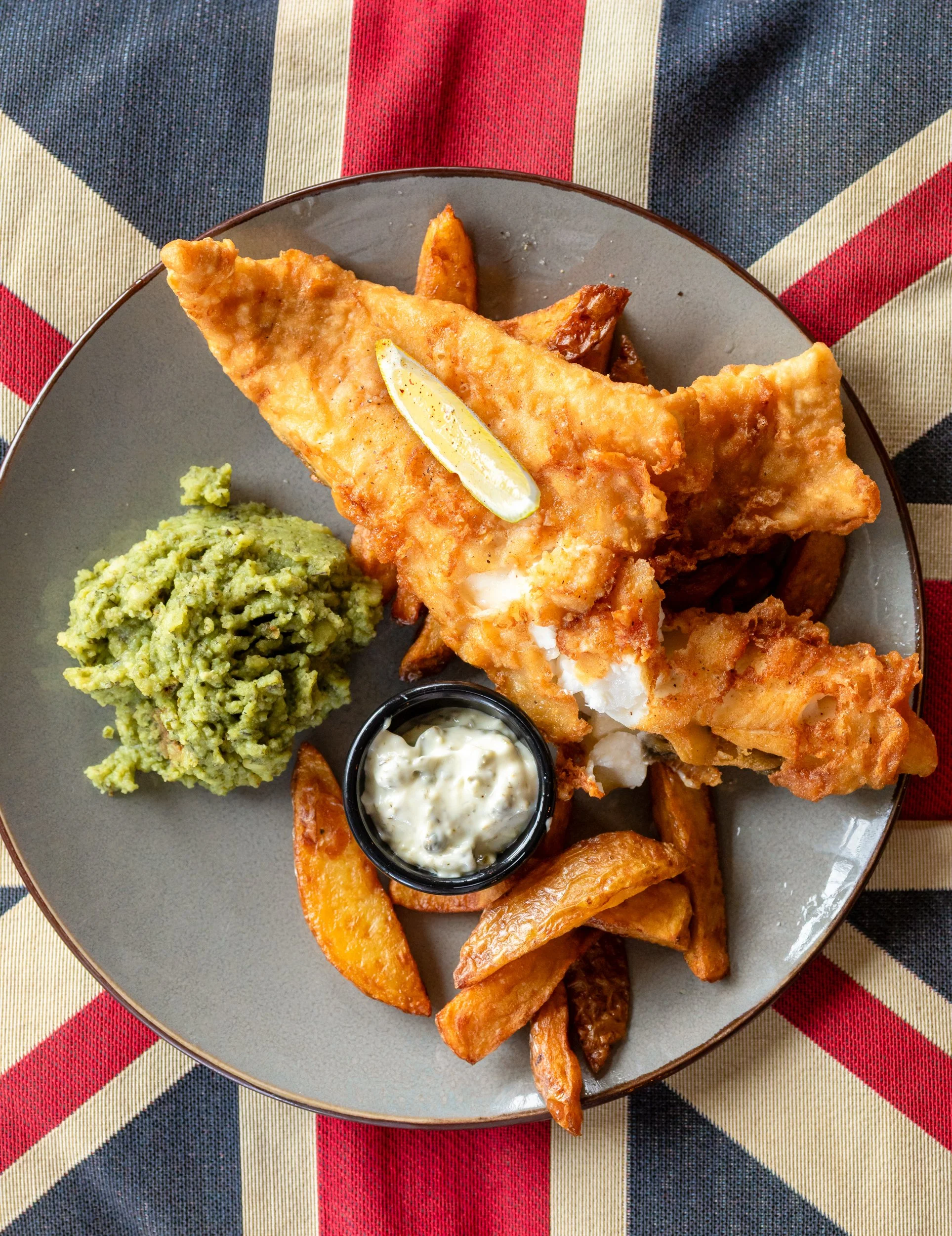 Traditional fish & chips with mushy peas on a Union Jack cushion at The Folly Wine Bar in Petersfield, Hampshire. Food photography by Sequoia Studios.