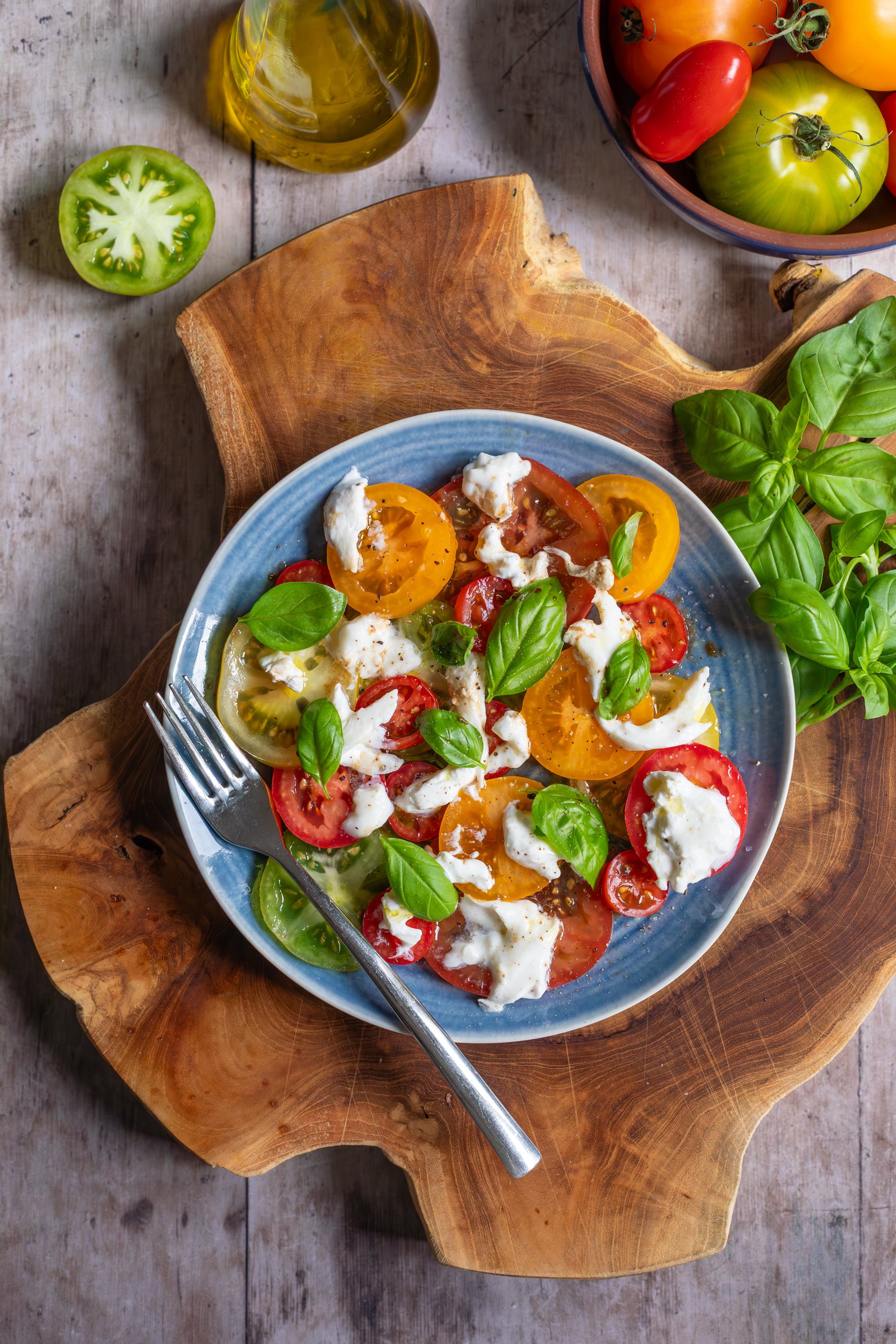 Tomato, burrata and basil salad on blue plate and wooden board