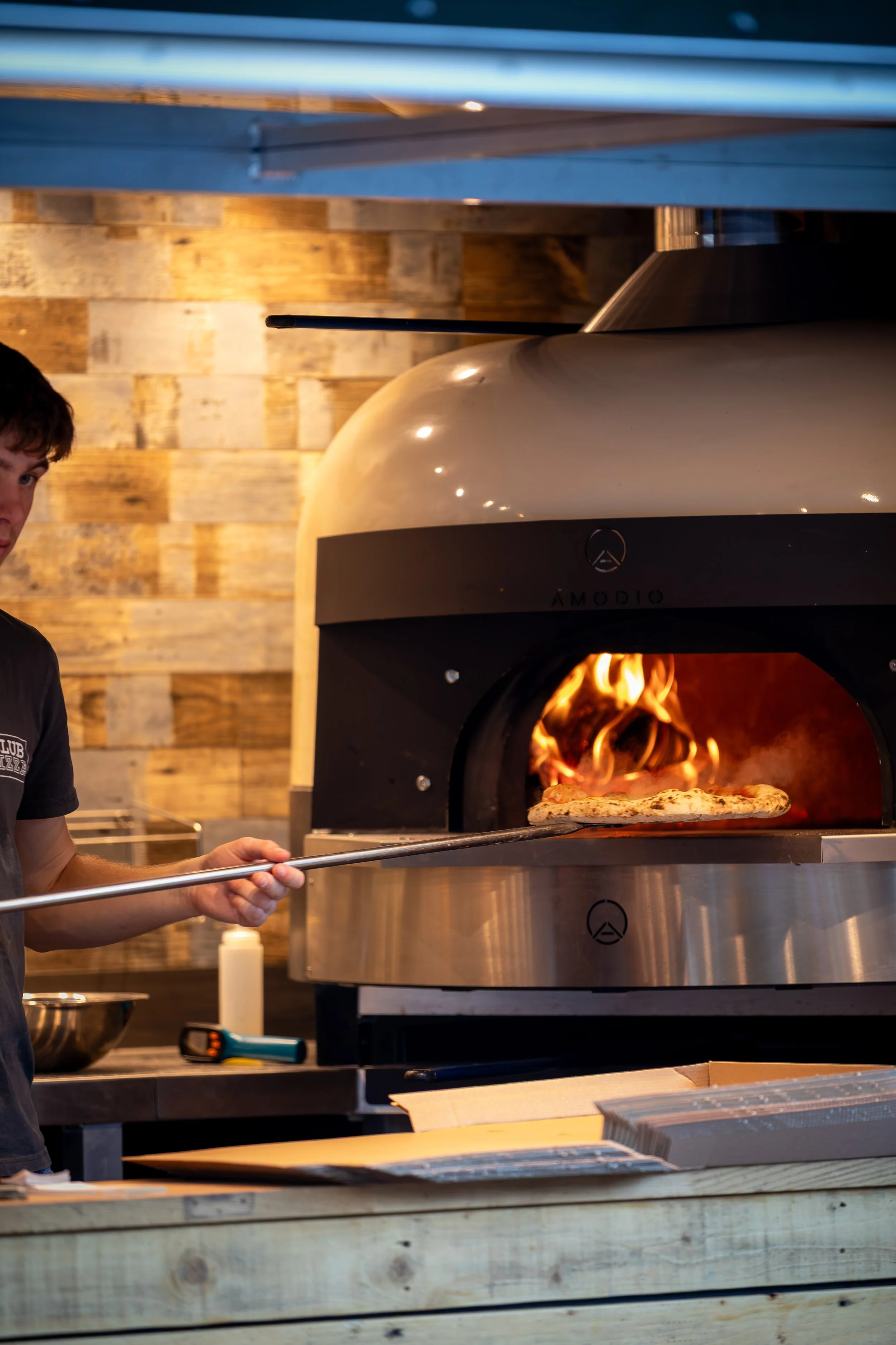 Staff member removing pizza from wood-fired oven at Club Pizza