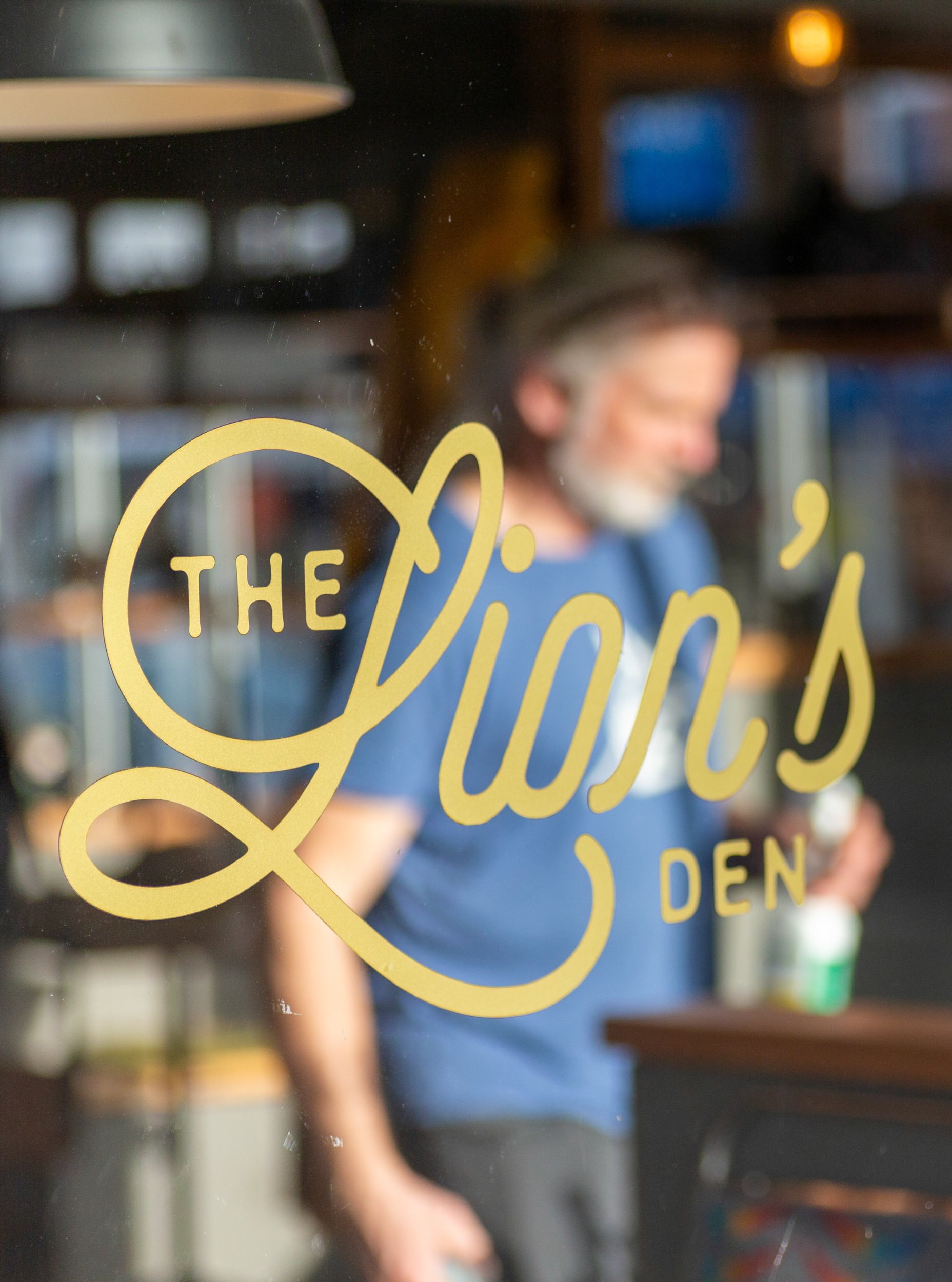 Café logo window decal with the proprietor blurred in background – The Lion's Den Café, Haslemere, Surrey – Hospitality Venue Photography by Sequoia Studios