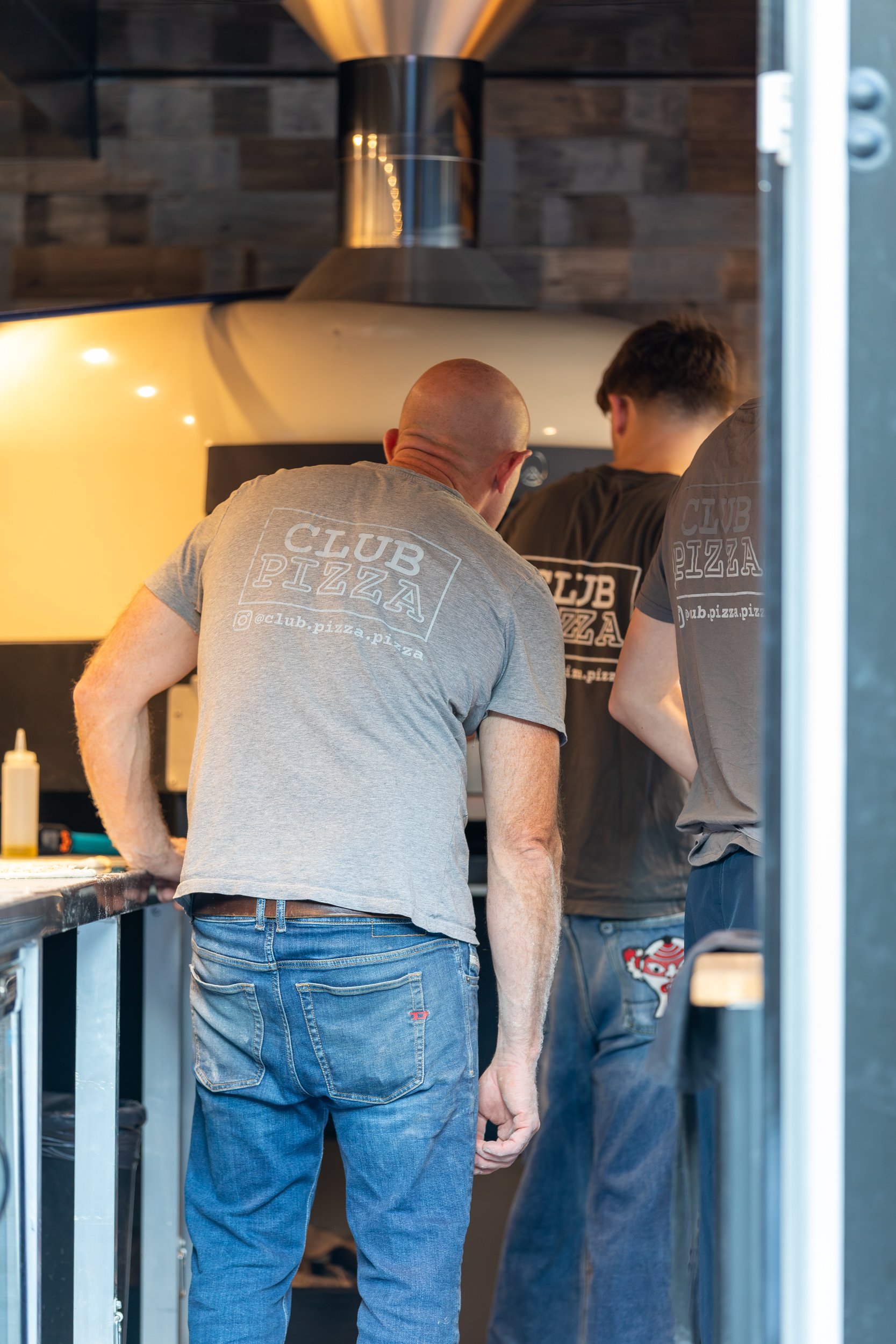 Owner and staff checking pizzas in wood-fired oven at Club Pizza
