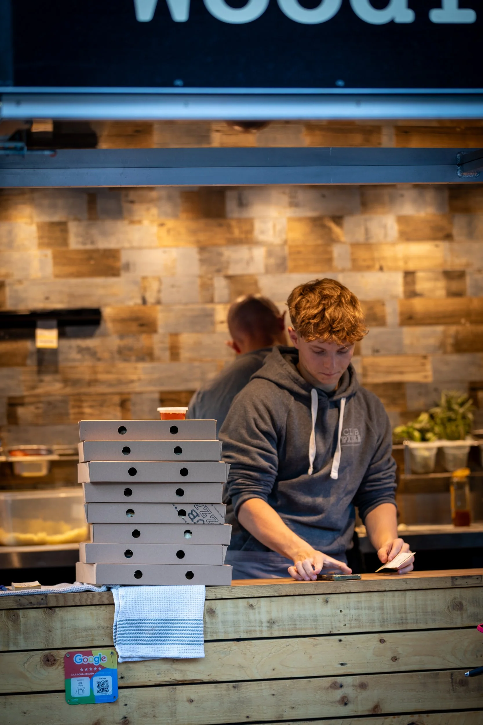 Club Pizza staff with stacked pizza boxes at The Crossways Inn, Churt, Surrey. Food & hospitality photography by Sequoia Studios