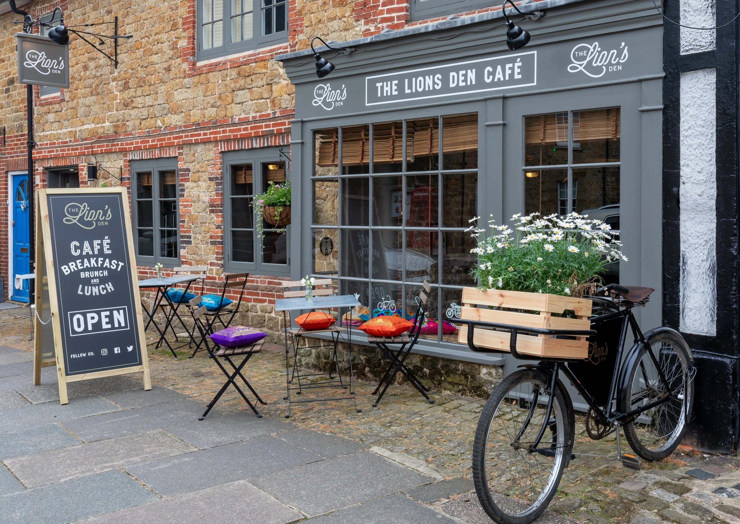 Exterior of The Lion's Den café in Midhurst, West Sussex with their signature branded delivery bike in foreground