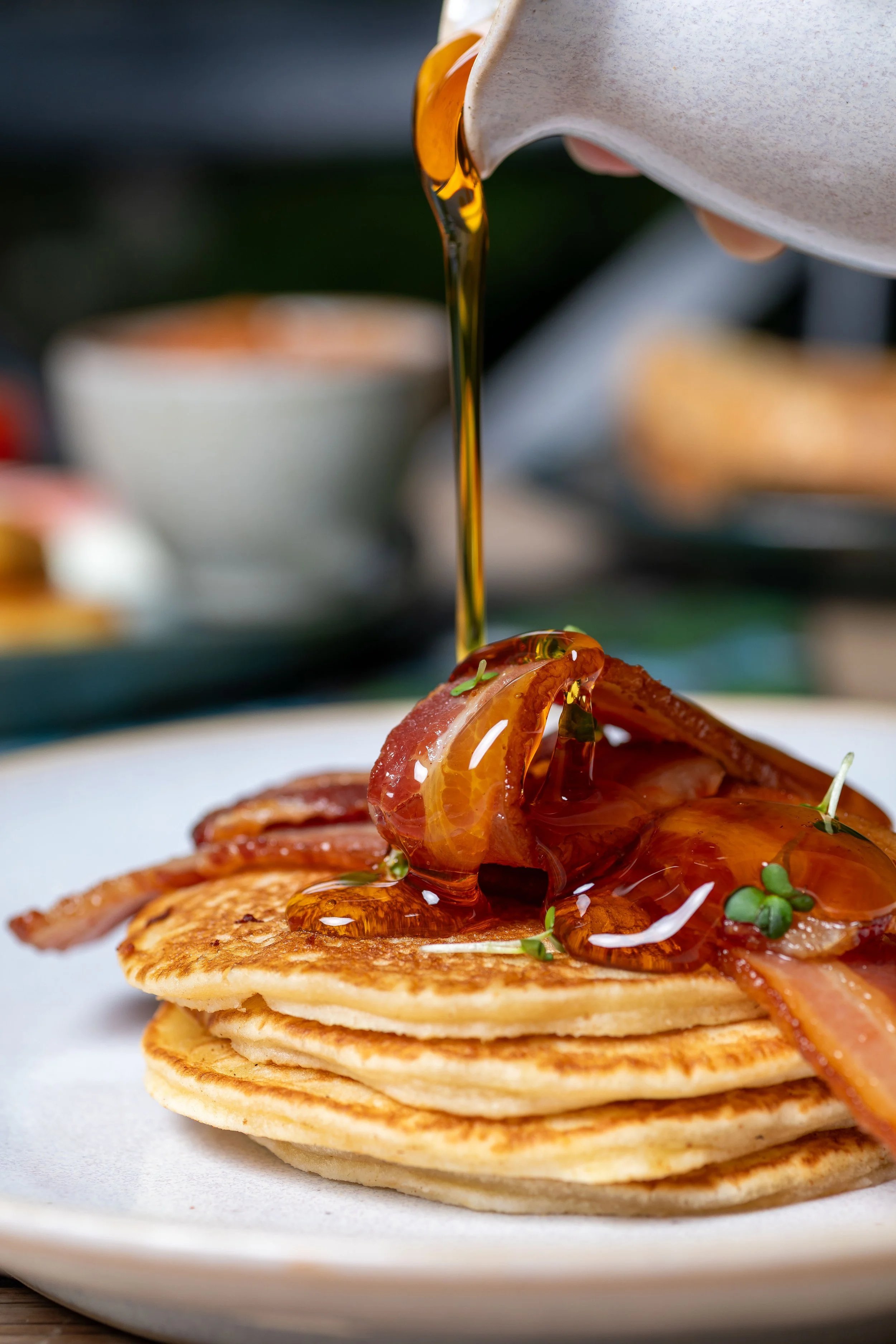 American style pancakes with bacon at The Kiln Cafe, with maple syrup being poured from a jug made at Grayshott Pottery