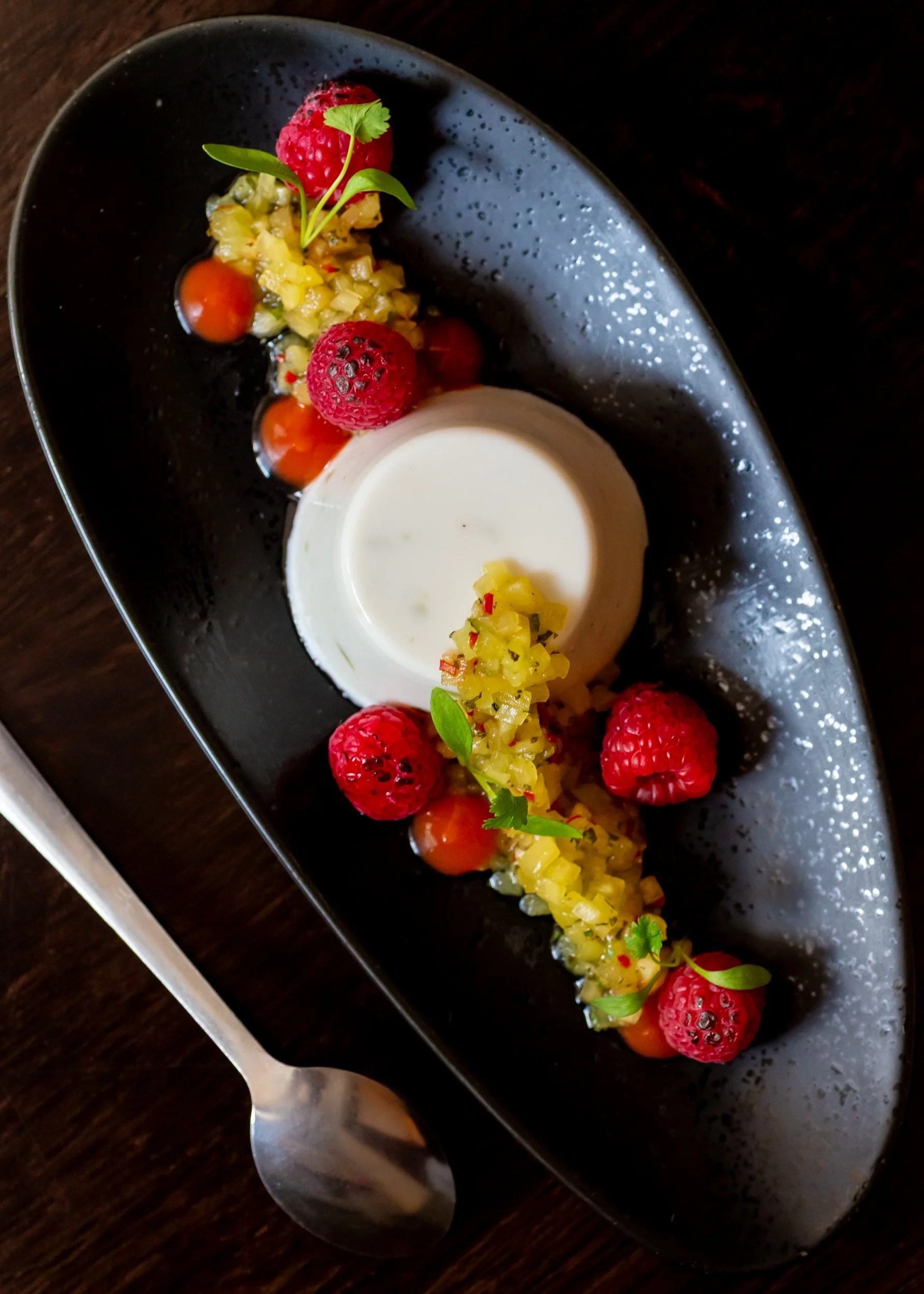 Classic vanilla panna cotta with seared pineapple salsa on black plate, shot from above at The Wheatsheaf Inn Grayswood, Surrey – Pub Food Photography by Sequoia Studios