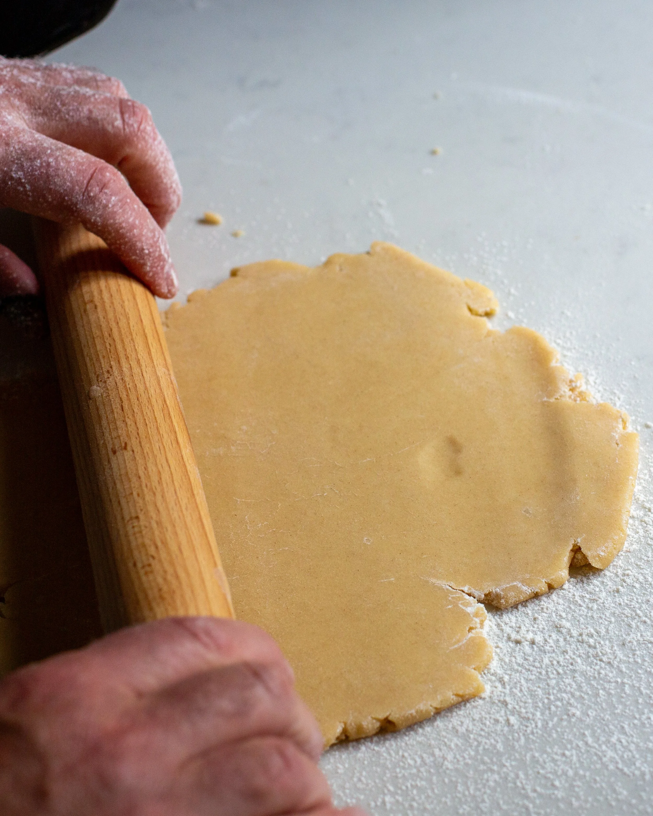 Man's hands using wooden rolling pin to rollout freshly made shortcrust pastry