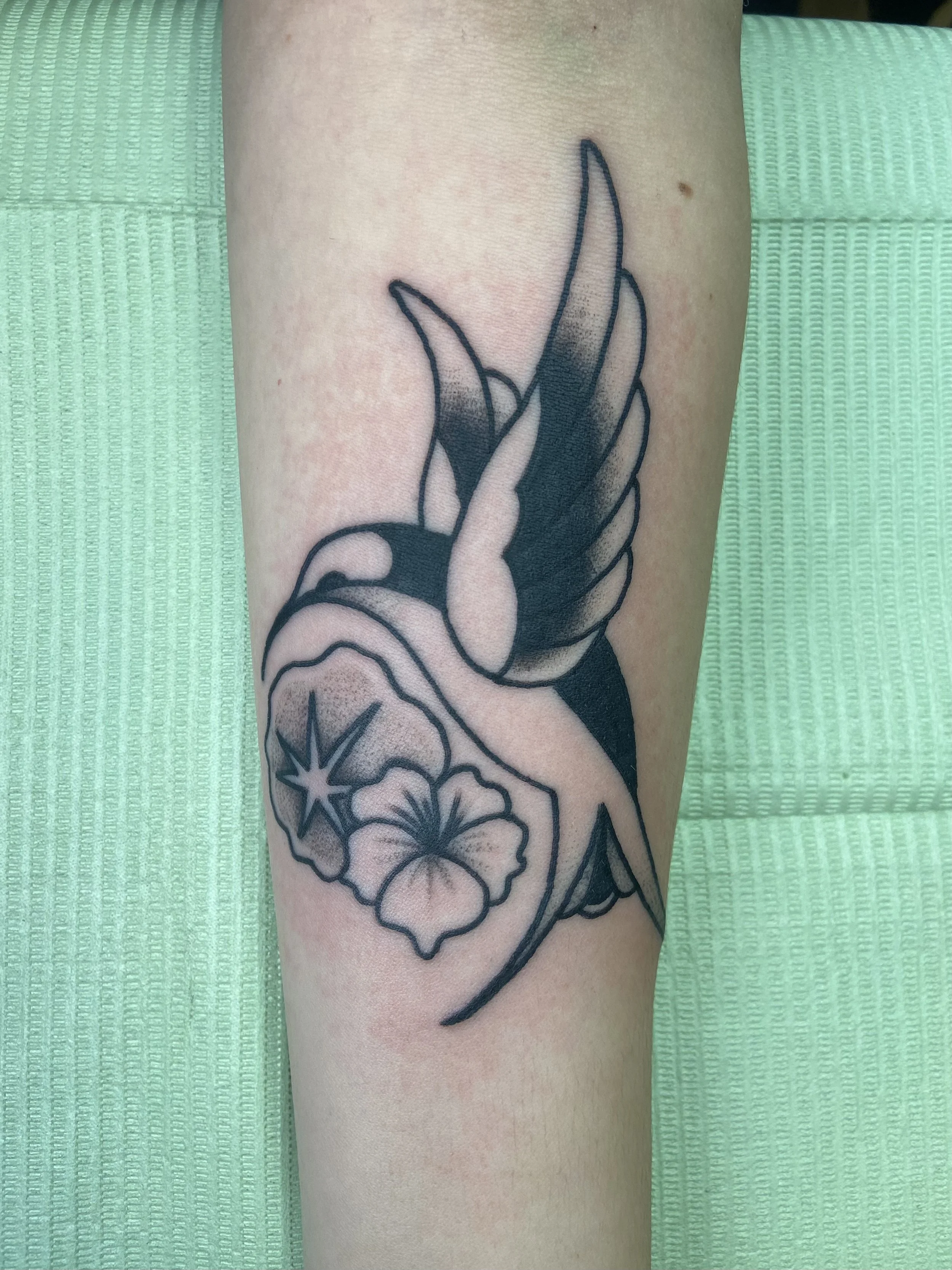 Tattoo of a hummingbird with flowers on person's leg
