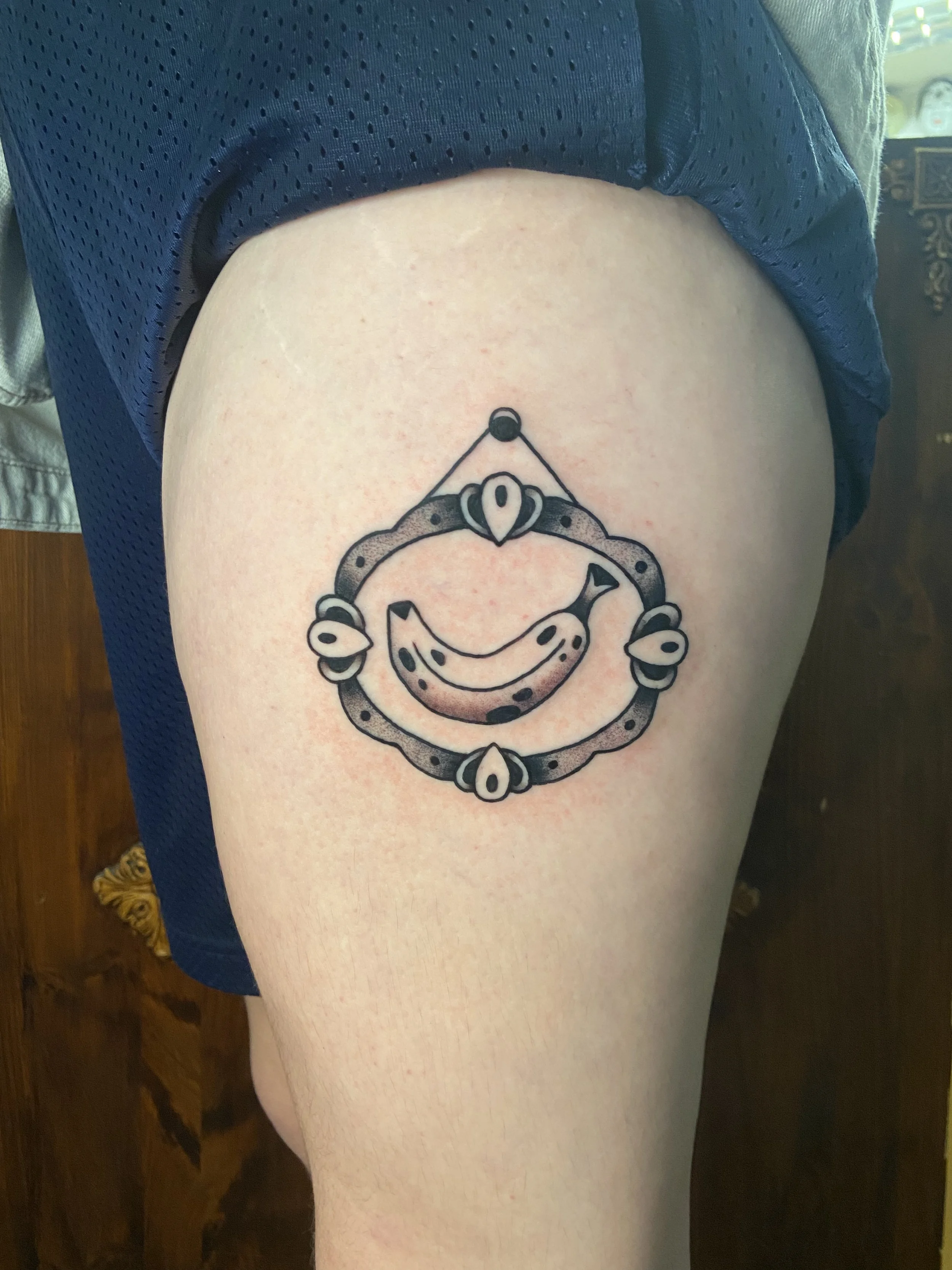 A tattoo on a person's upper thigh depicting a circular frame with a smiling snake inside.