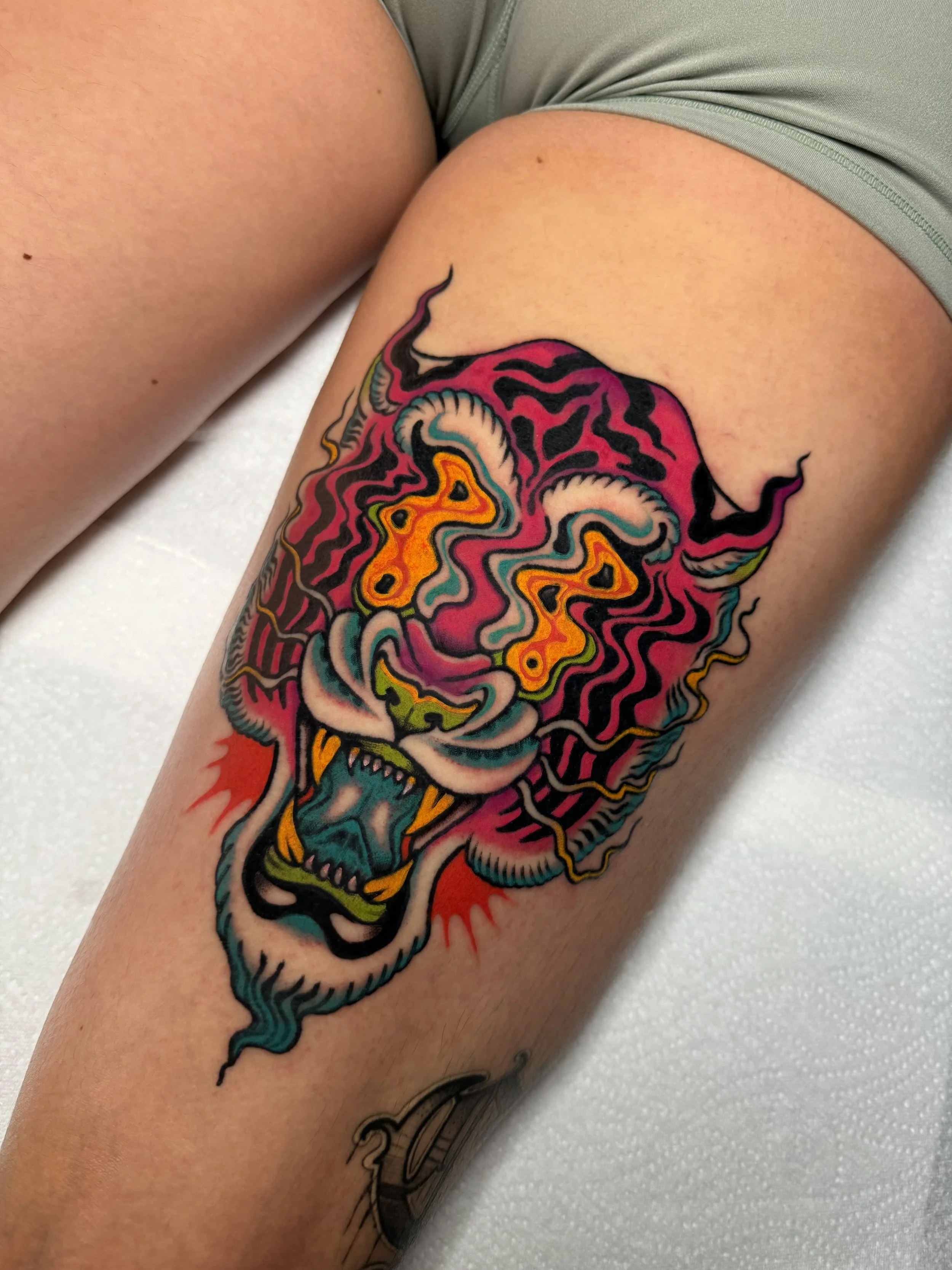 Colorful tattoo of a fierce tiger's face with abstract and flowing patterns, on a person's thigh. Trippy and Psychedelic colourful tattoo