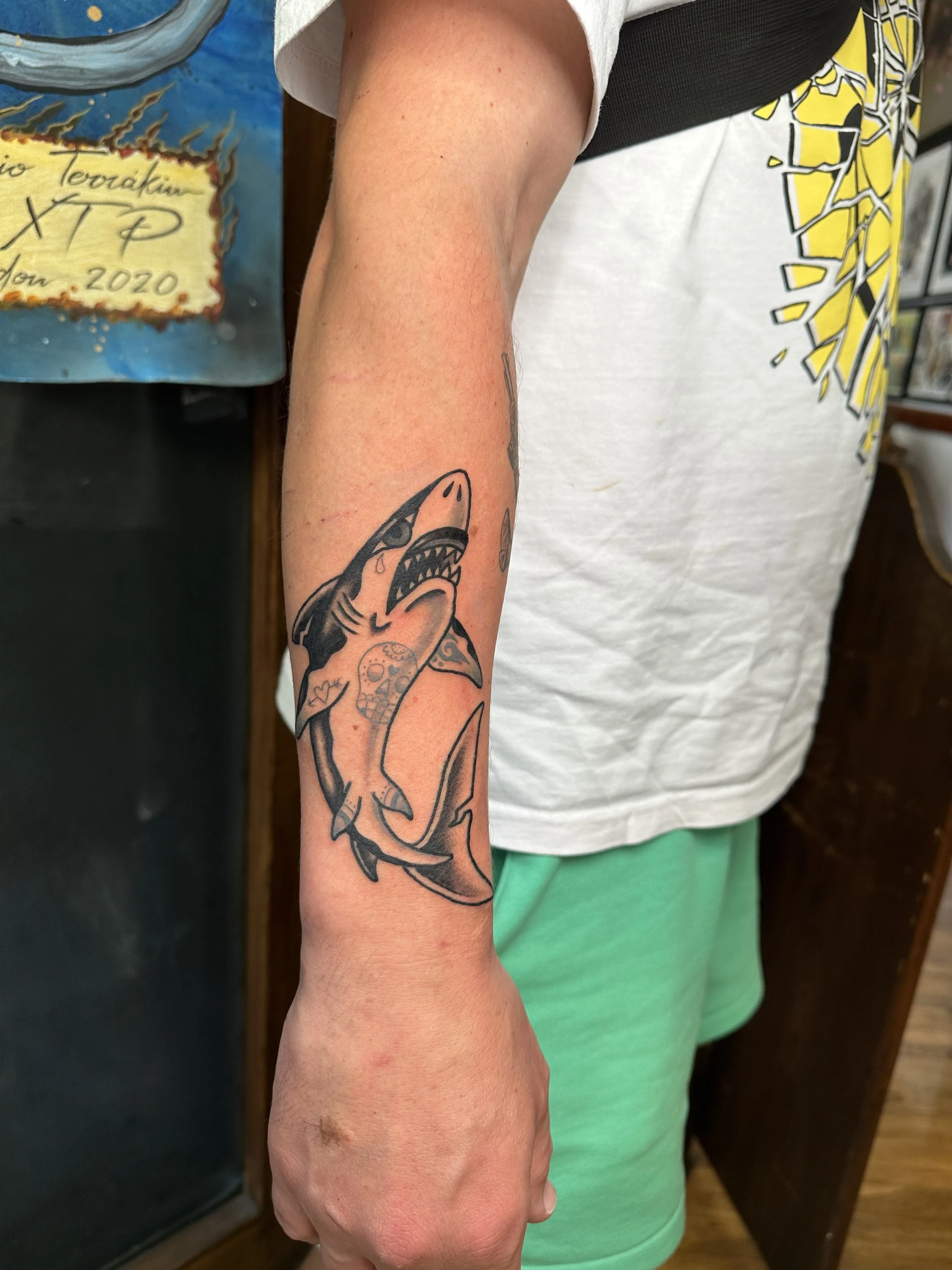 Tattoo of a shark with various decorative elements on a person's forearm.