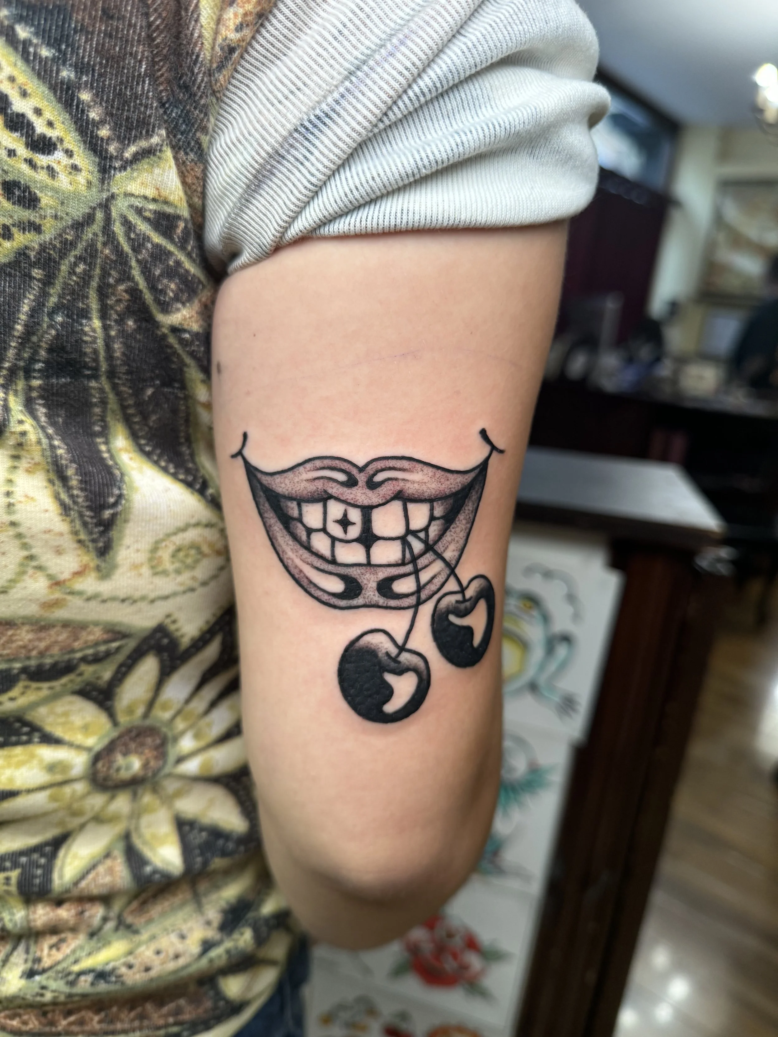 Tattoo of a smiling mouth with cherry handing out of it. Black traditional tattoo.