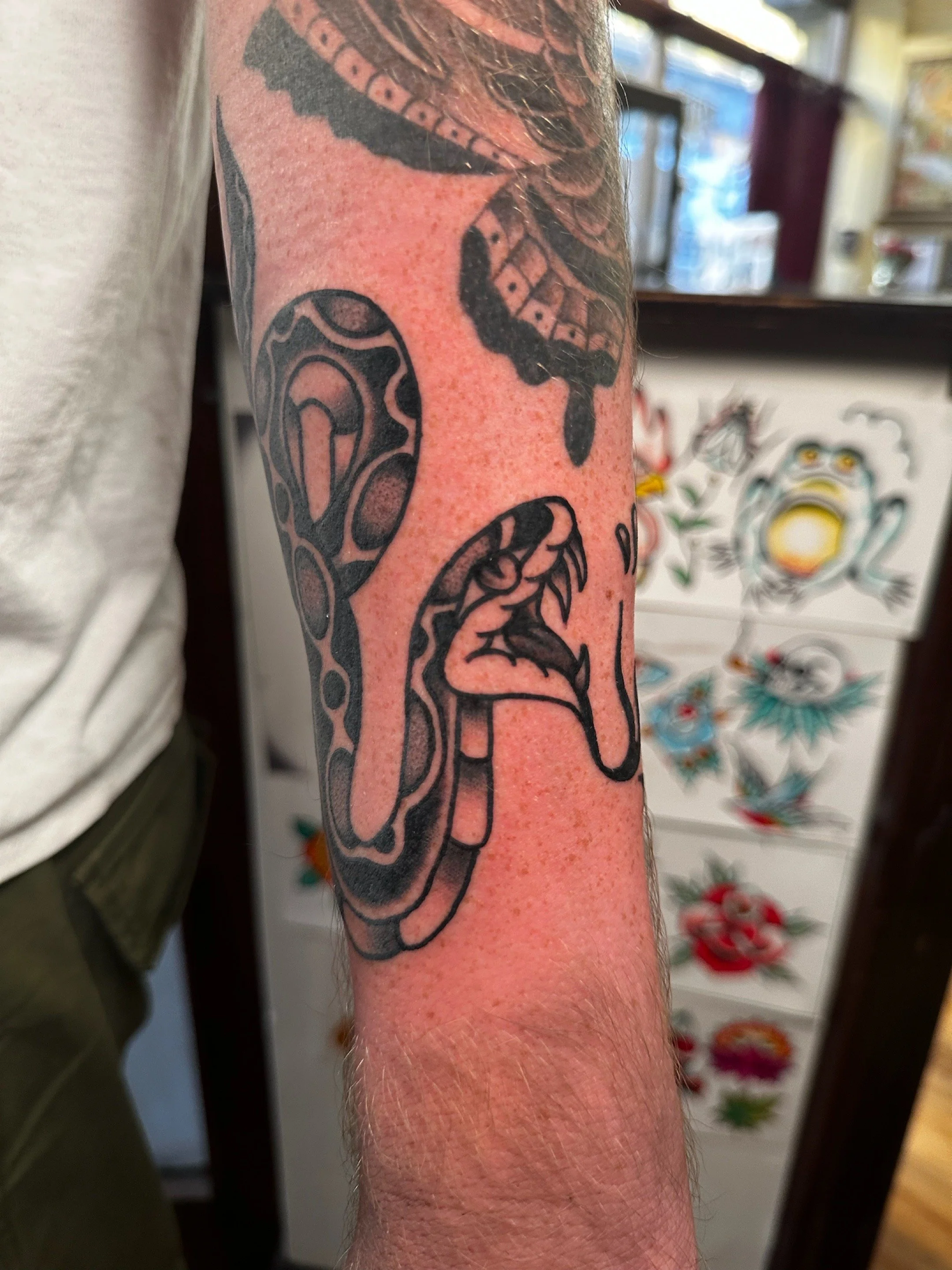 Tattoo of a snake's head with its mouth open on a person's forearm.
