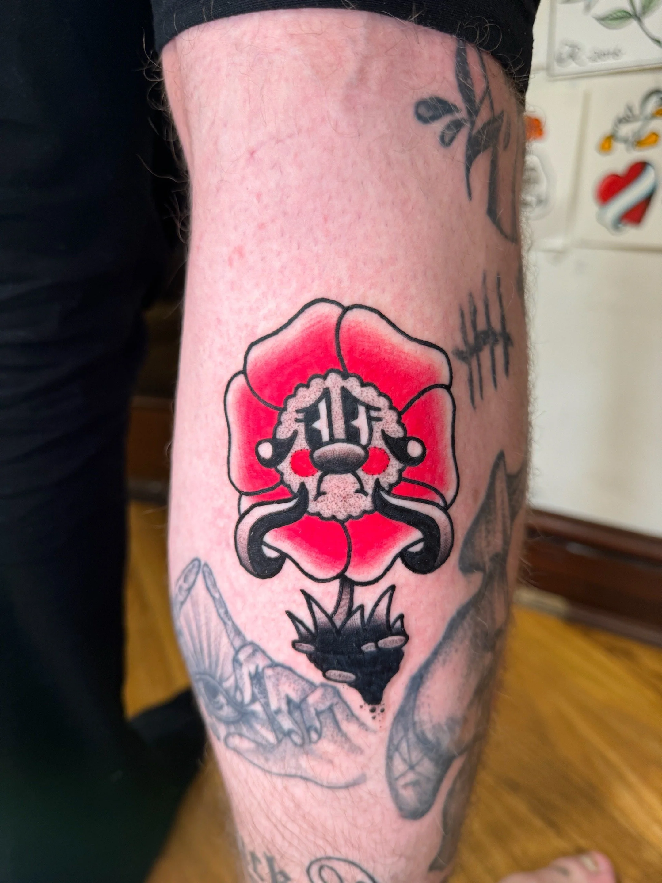 Tattoo of a sad cartoon face red flower on a leg.