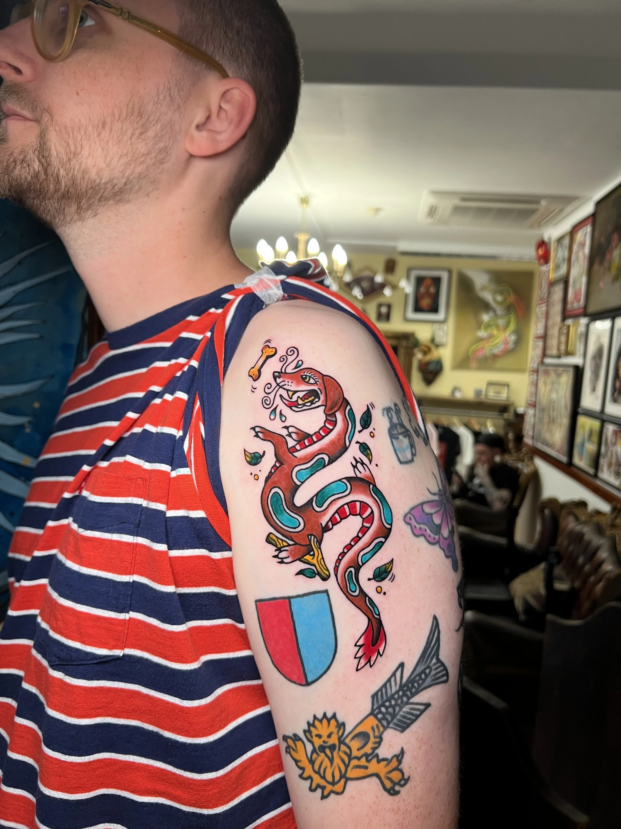 Tattoo of a stylized dragon that is based off of his daschound on a person's upper arm.