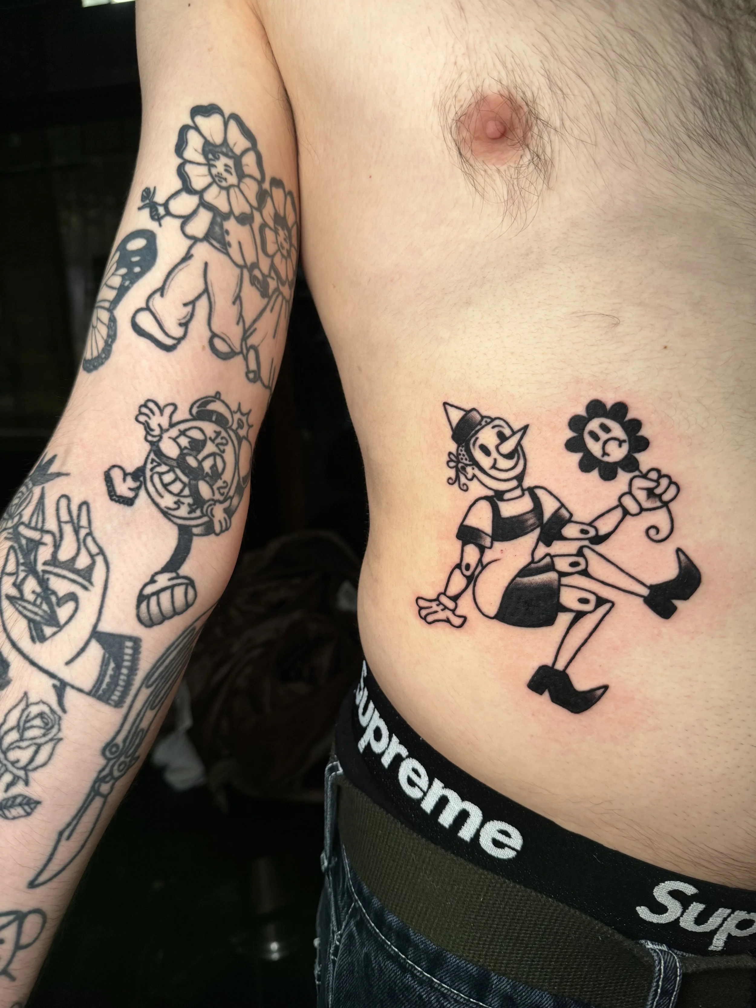 Tattoo of Pinocchio holding a flower on the side of a person's torso.