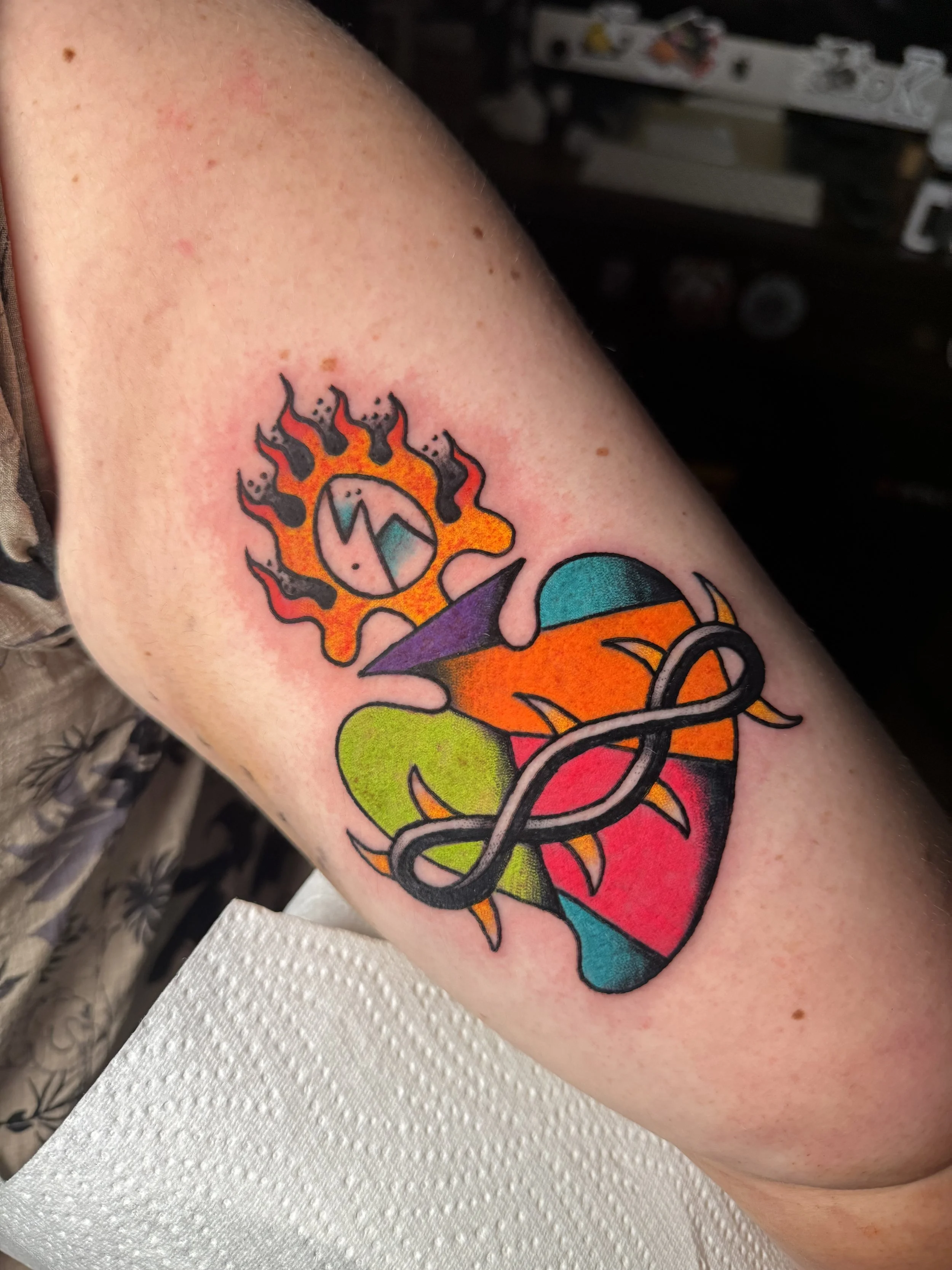 Colorful tattoo of a traditional sacred heart on arm featuring an egg, fire and thorns.