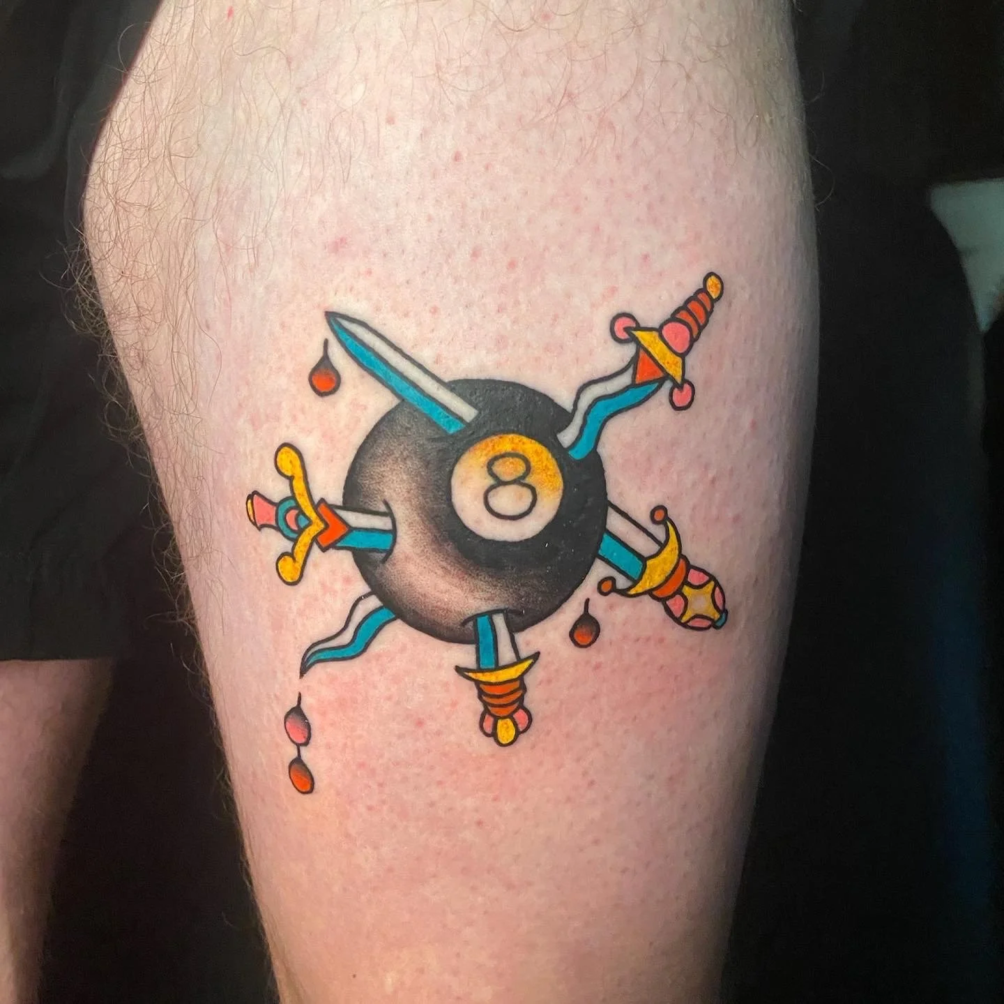 Colorful tattoo of a black billiard ball with the number 8 holding four cartoonish swords, each with a different colored hilt, and drops of red liquid dripping from the sword tips.